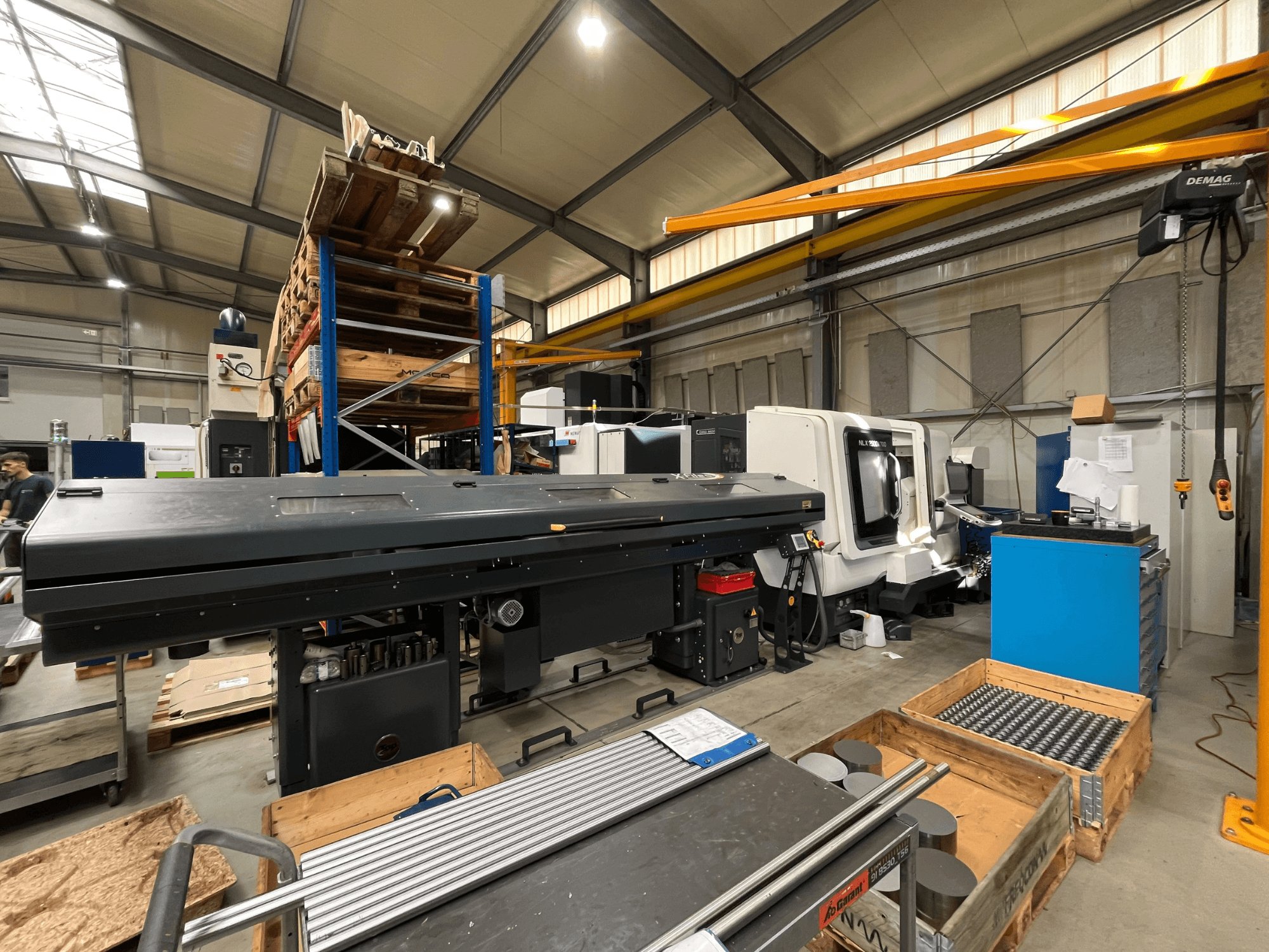 Горизонтальный токарный станок DMG MORI MORI NLX 2500/700 SY в цехе, вид сбоку; на заднем плане — склад и инструменты.