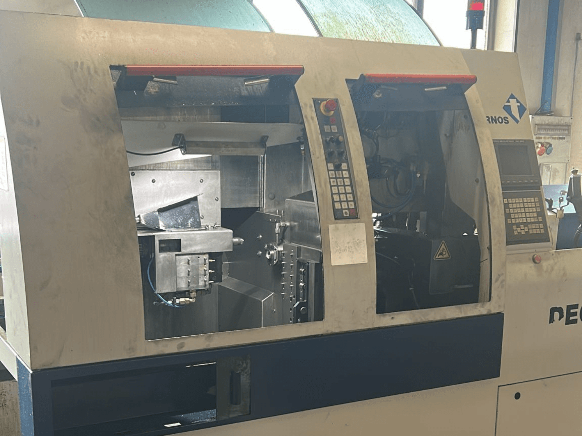 Alt text: Вид спереди на токарный станок швейцарского типа TORNOS Deco 13 b, видны панели управления и внутренние компоненты.