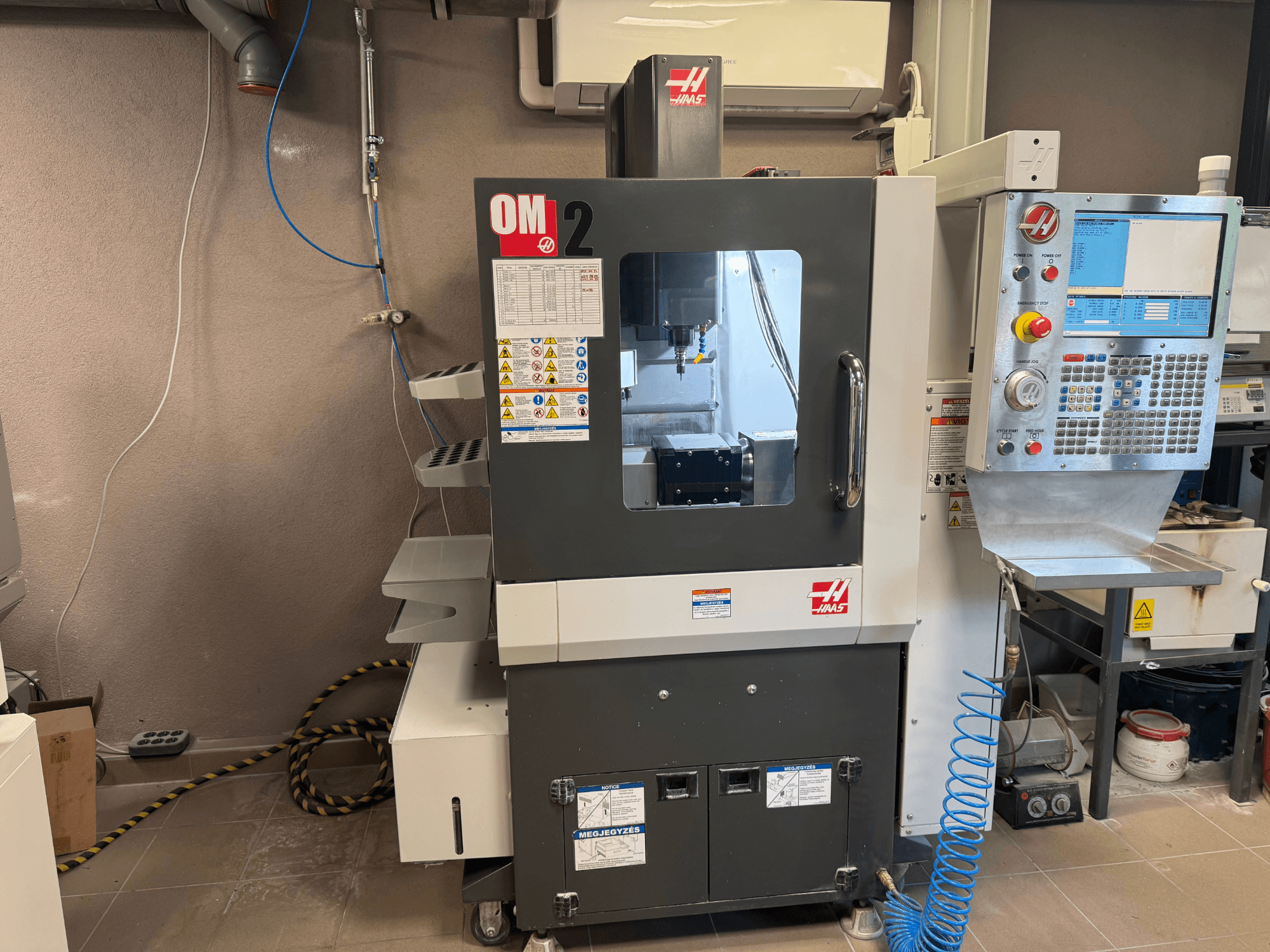 Станок с ЧПУ Haas OM-2, вид спереди, панель управления, шпиндель и знаки безопасности, установлен в мастерской.
