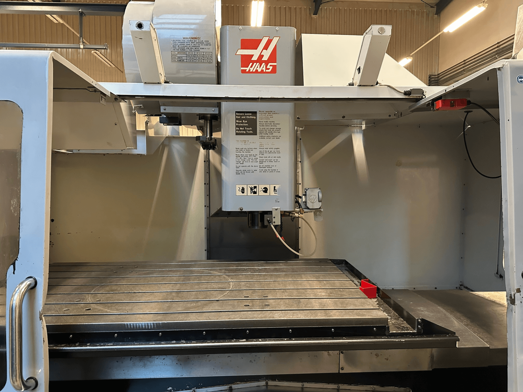 Фрезерный станок с ЧПУ Haas, модель VF-2, вид спереди, демонстрирующий органы управления, металлический рабочий стол и табличку безопасности на панели.