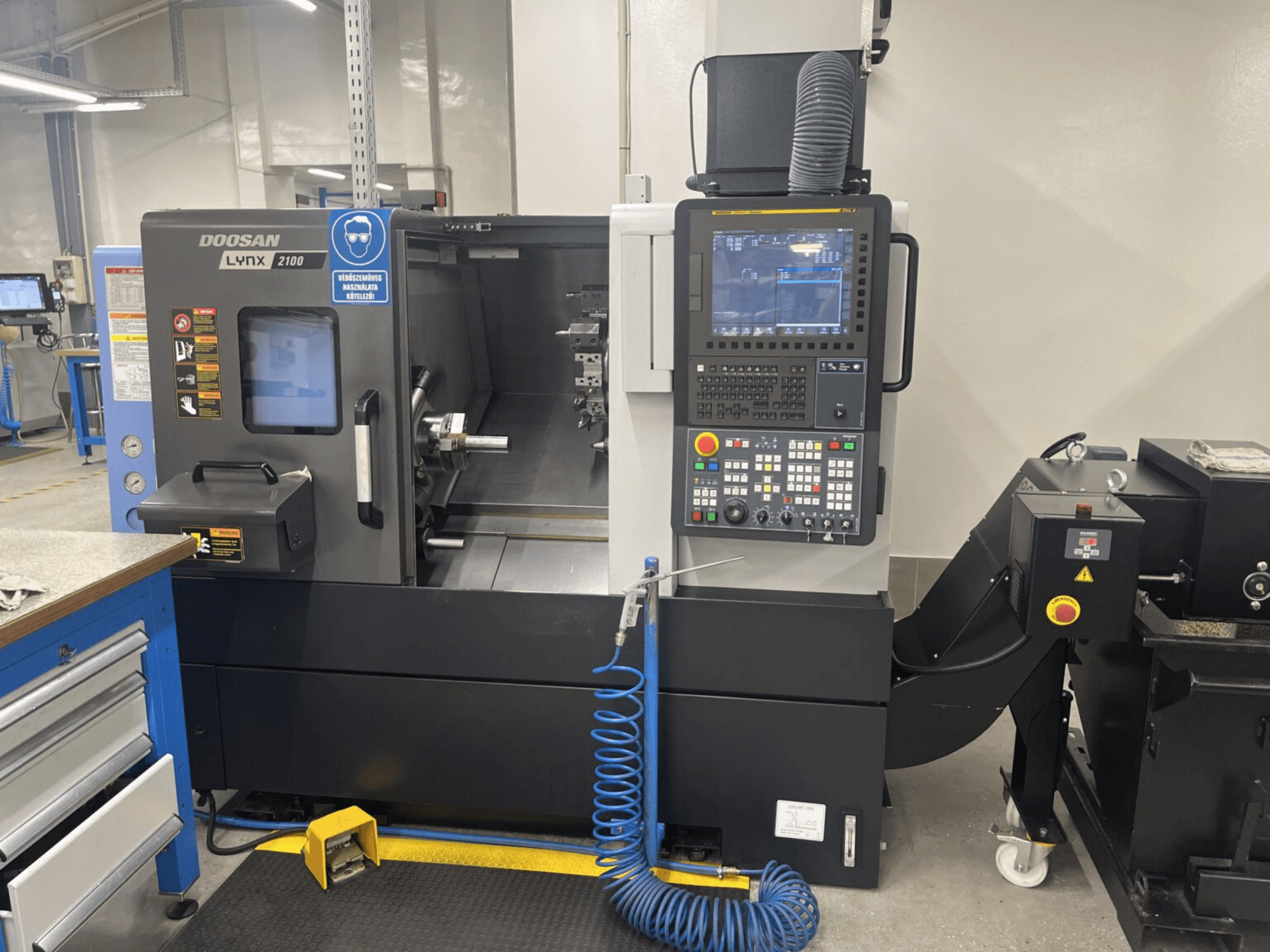 Вид спереди горизонтального токарного станка DOOSAN Lynx 2100A, демонстрирующий панель управления и шпиндельную зону с заметными элементами безопасности.