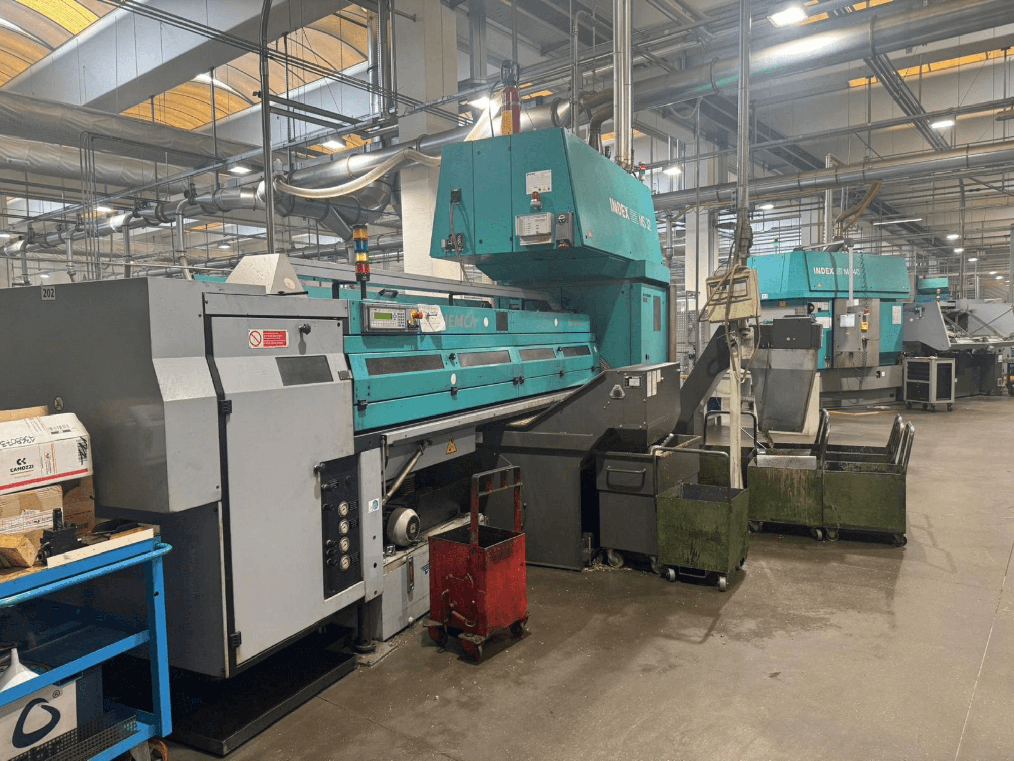 Многошпиндельный токарный станок INDEX MS32C, вид спереди, демонстрирующий органы управления и рабочую зону в мастерской.