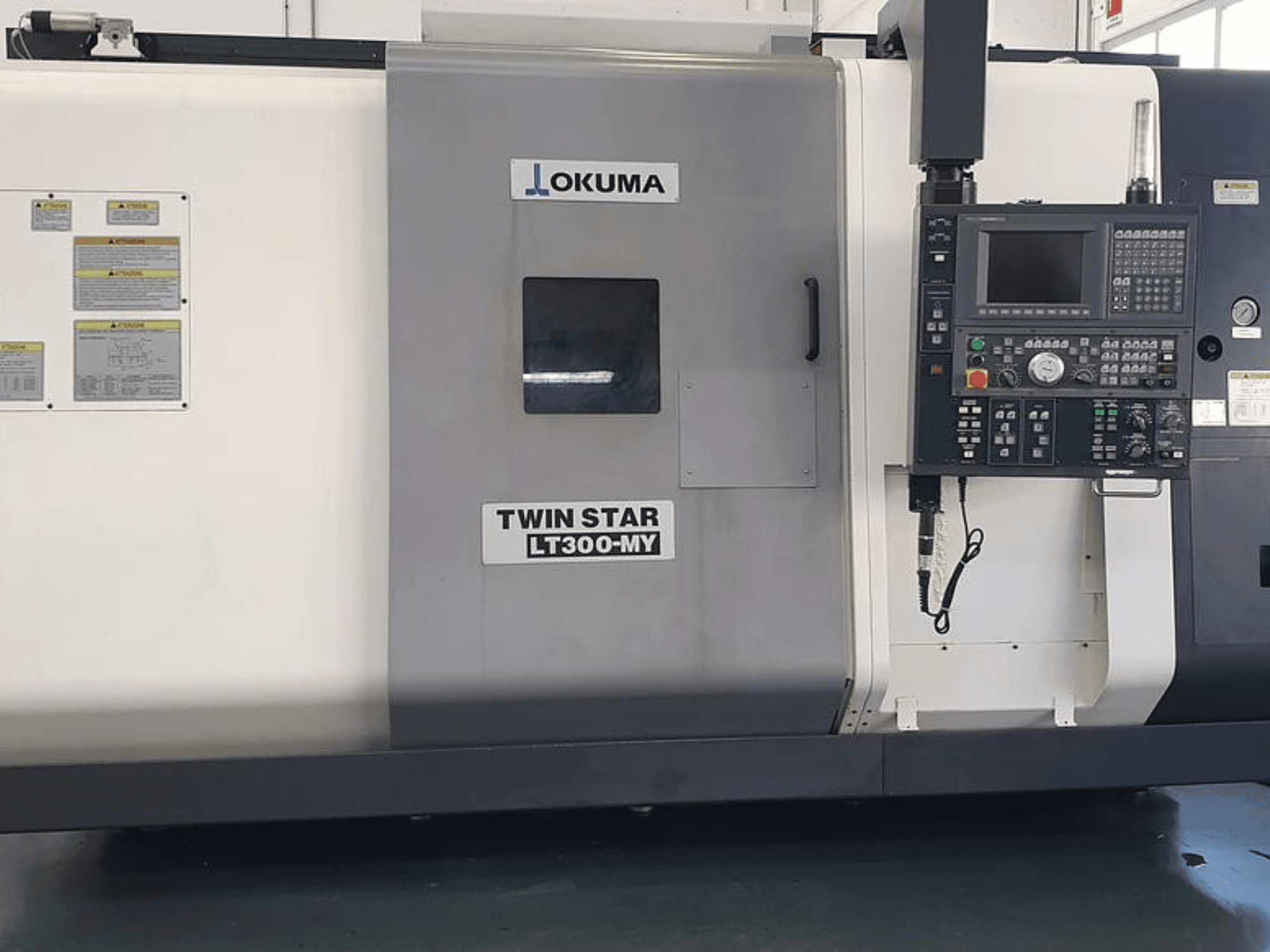 Токарный станок с ЧПУ Okuma Twin Star LT300-MY вид сбоку, панель управления, кнопки управления и знаки безопасности.