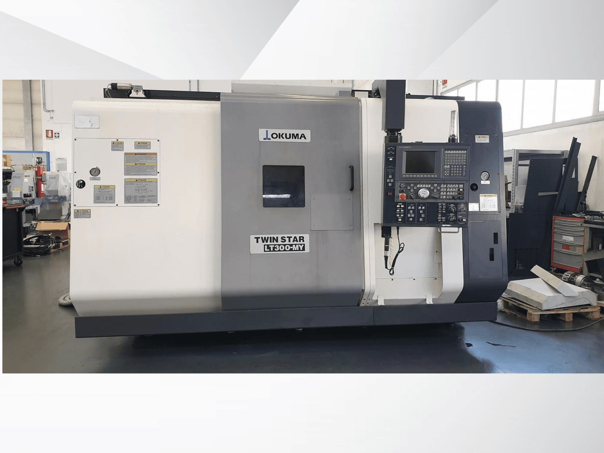 Токарный станок с ЧПУ Okuma Twin Star LT300-MY, вид спереди, видна панель управления и рабочие наклейки.