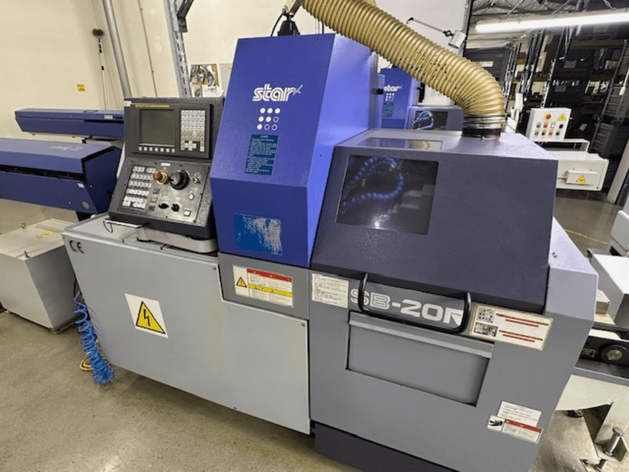 Токарный станок Star SB-20R типа N швейцарского типа, вид спереди, панель управления, всасывающий шланг и видимые символы опасности.