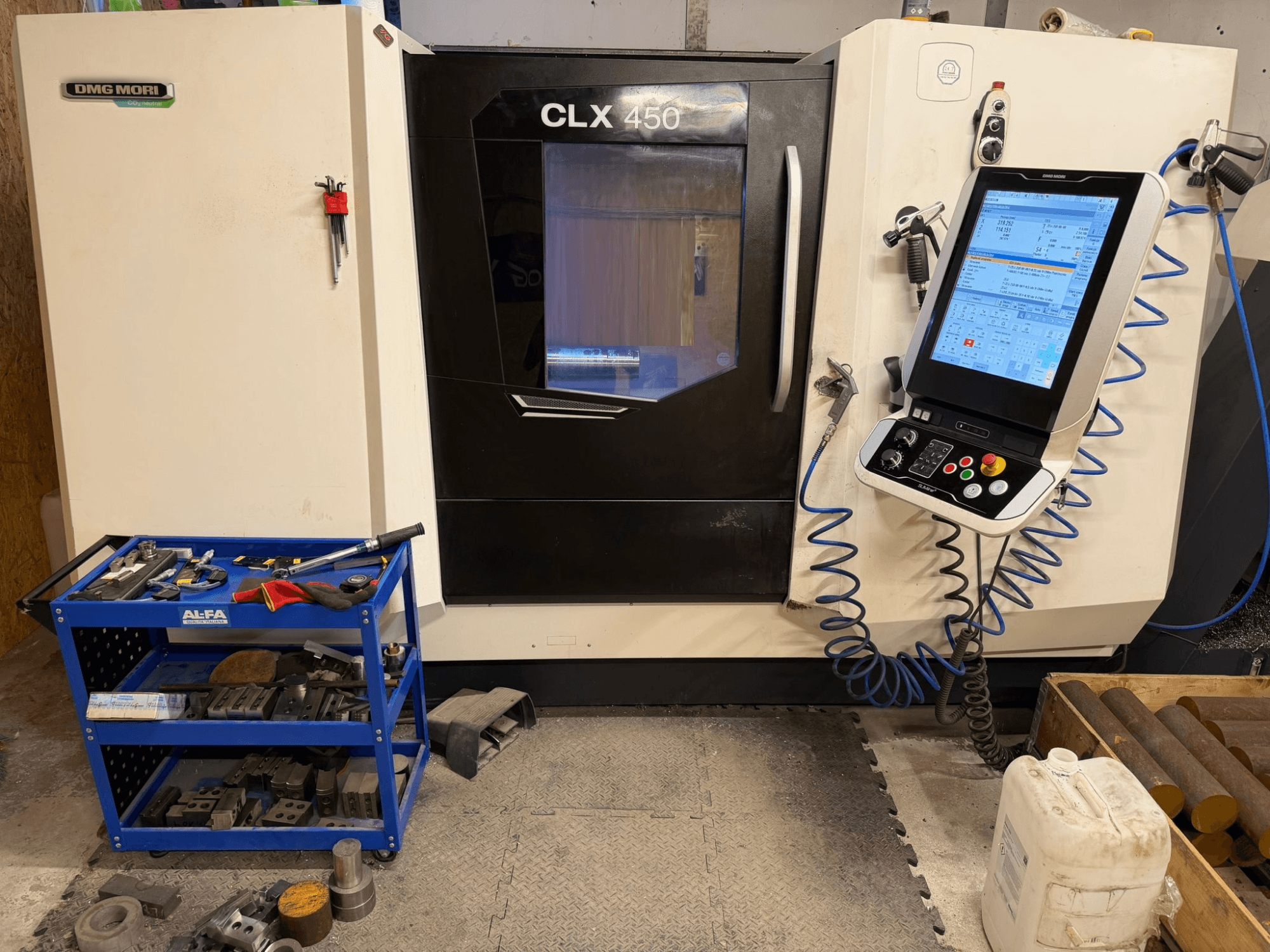Горизонтальный токарный станок DMG MORI CLX 450 V3 вид спереди, панель управления и расположенная рядом инструментальная тележка с оборудованием.