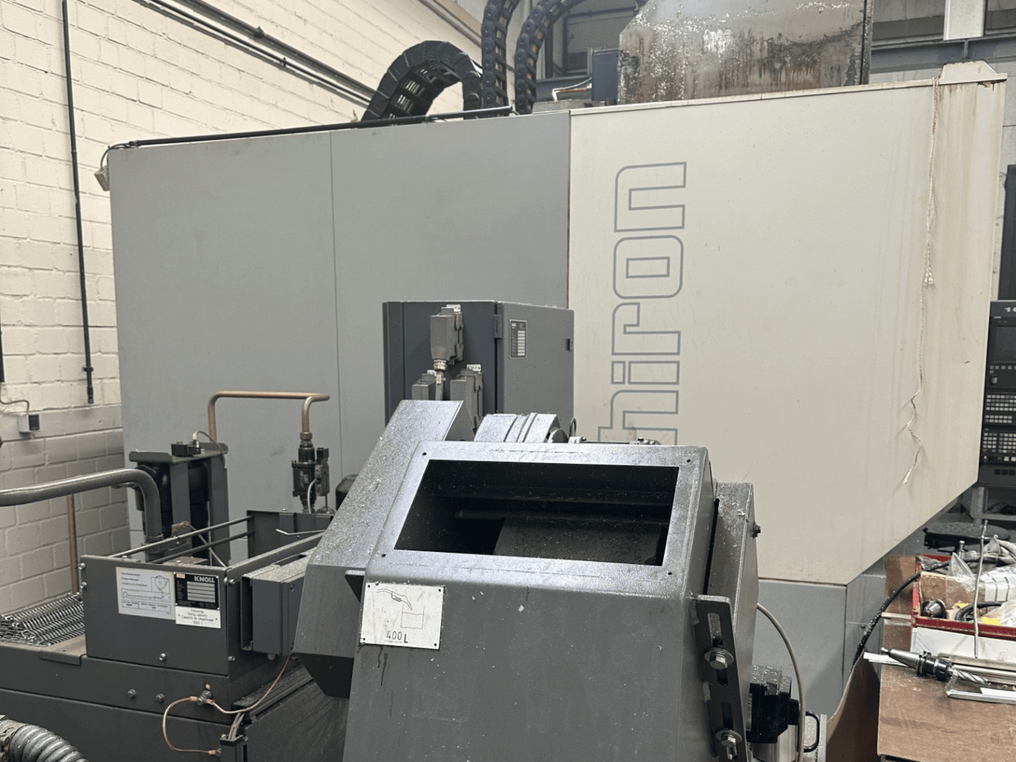 Брэнд: Chiron; Вид спереди на промышленный станок с ЧПУ с серым внешним видом, видна панель управления, в фокусе - компоненты станка.