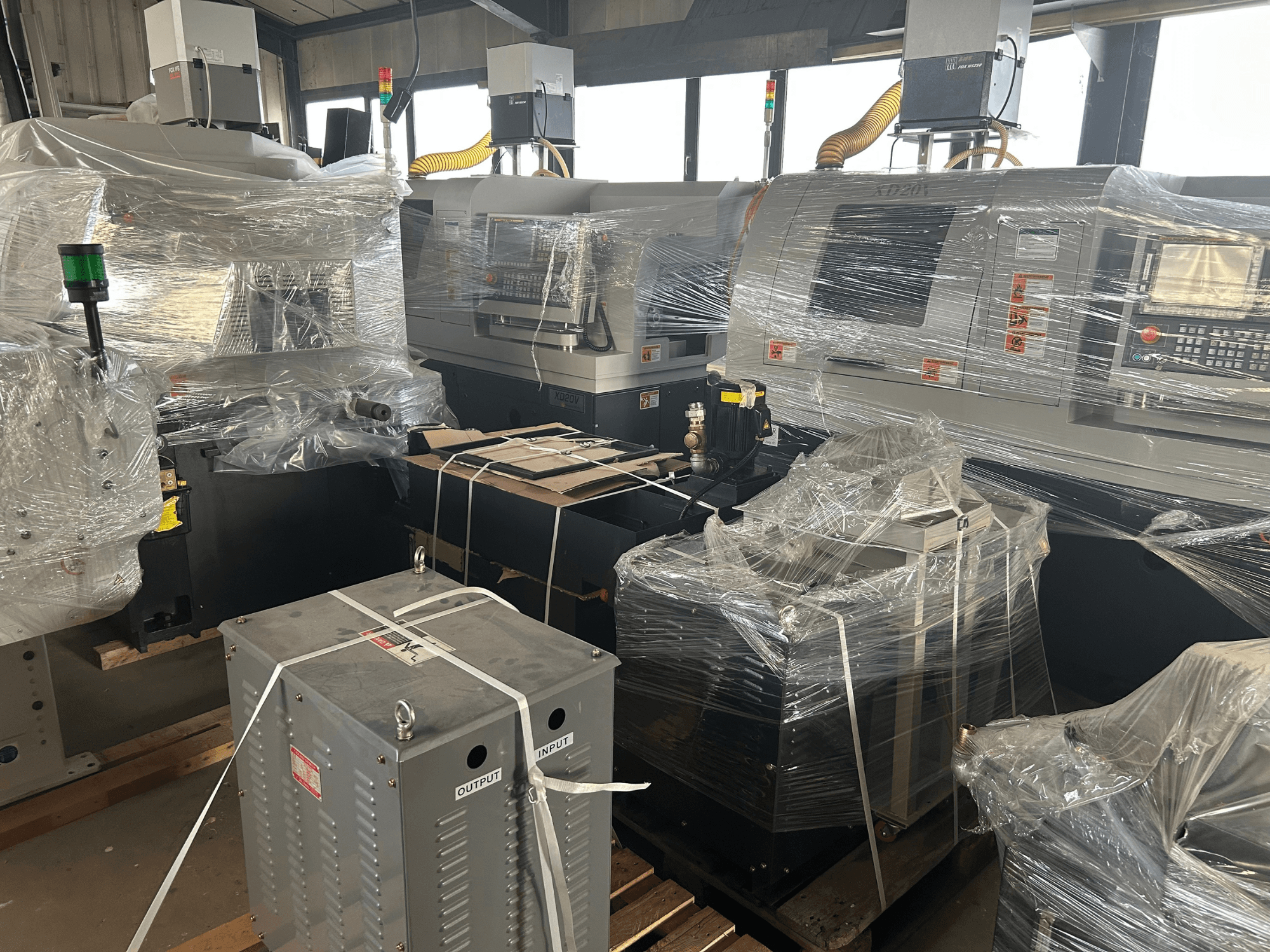 Комбинированный токарный станок Hanwha XD20V швейцарского типа, частично упакованный, показан с бокового ракурса, видны органы управления и компоненты оборудования.