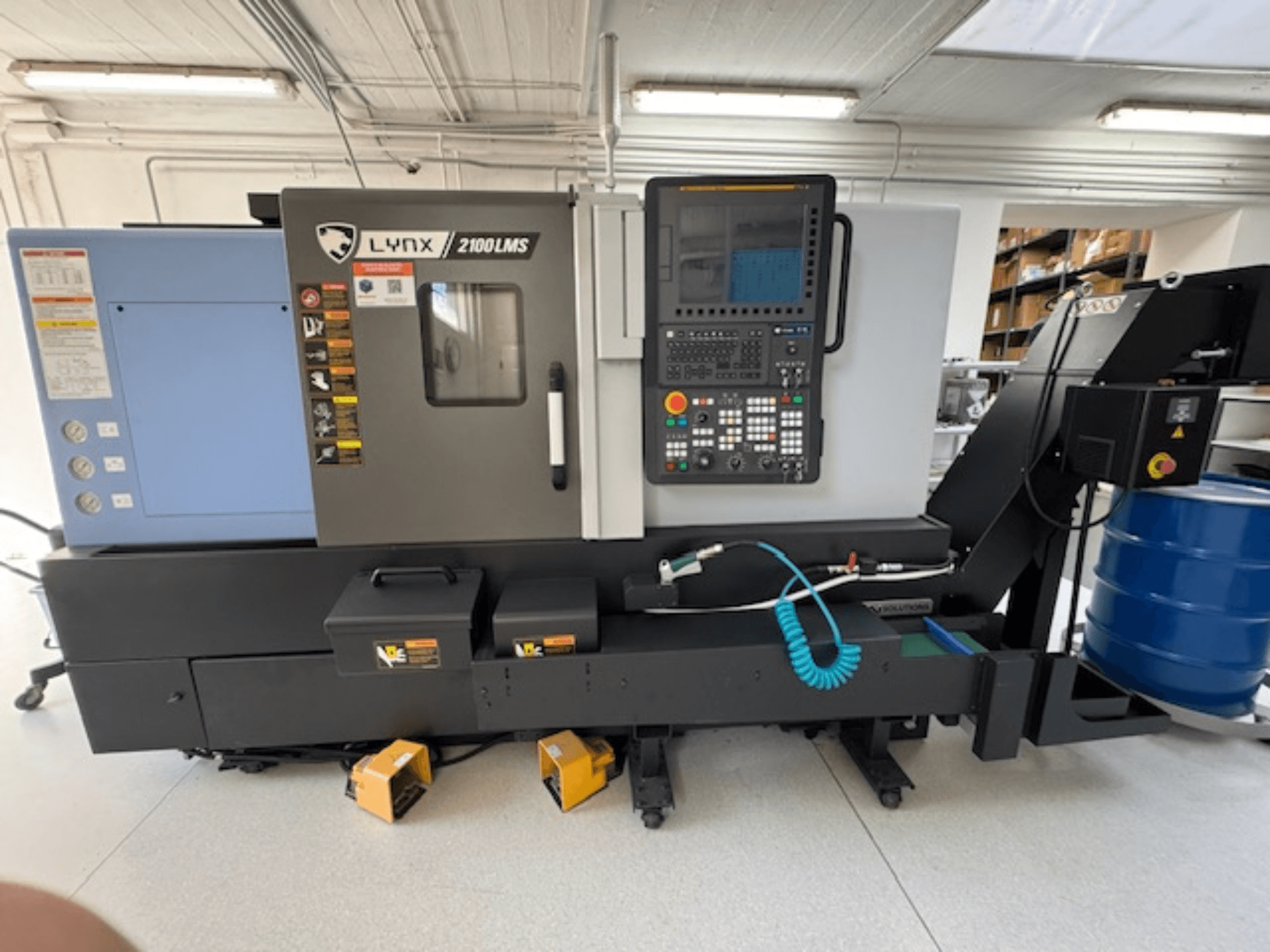 Горизонтальный токарный станок DOOSAN LYNX 2100LMSA, вид спереди, панель управления, шланг подачи охлаждающей жидкости и ящики для хранения.