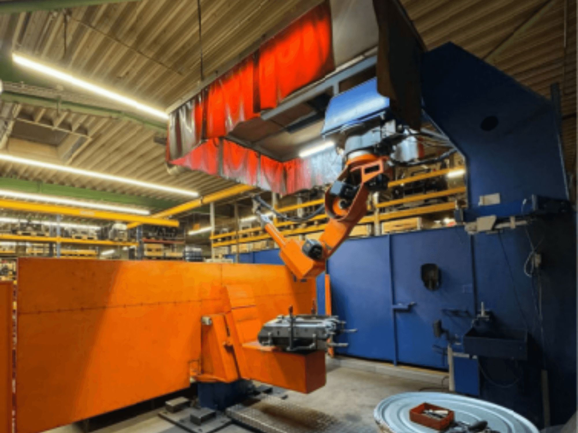Сварочный робот CLOOS Romat 350 e в промышленных условиях, вид спереди с оранжевой рукой, удерживающей заготовку под навесом.