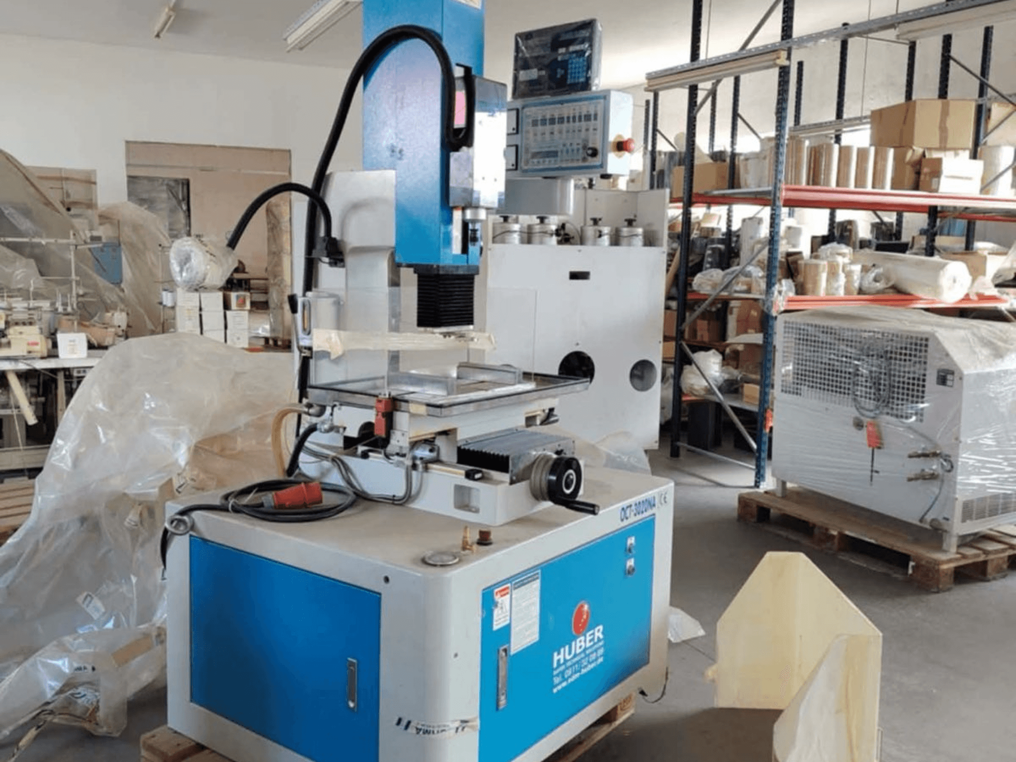 Станок HUBER OCT-3020 NA для электроэрозионной обработки давлением в мастерской, вид спереди, на котором видны сине-серый корпус, цифровые элементы управления и рабочая зона.