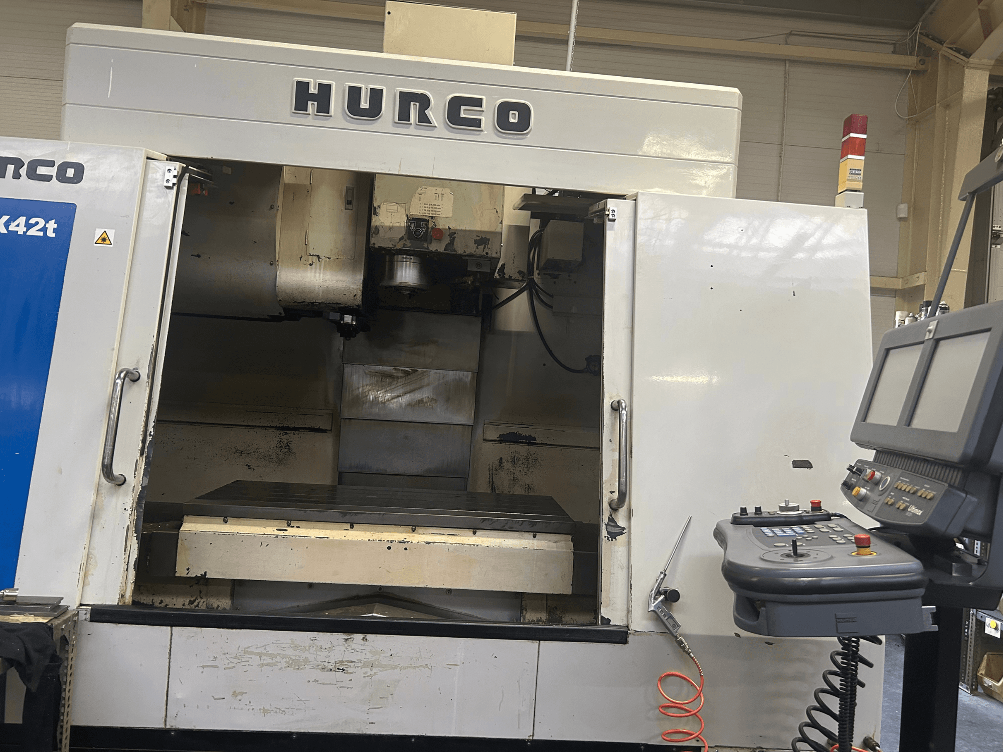 Фрезерный станок с ЧПУ Hurco VMX42T с видом спереди, с открытой рабочей зоной и панелью управления с кнопками и дисплеем.
