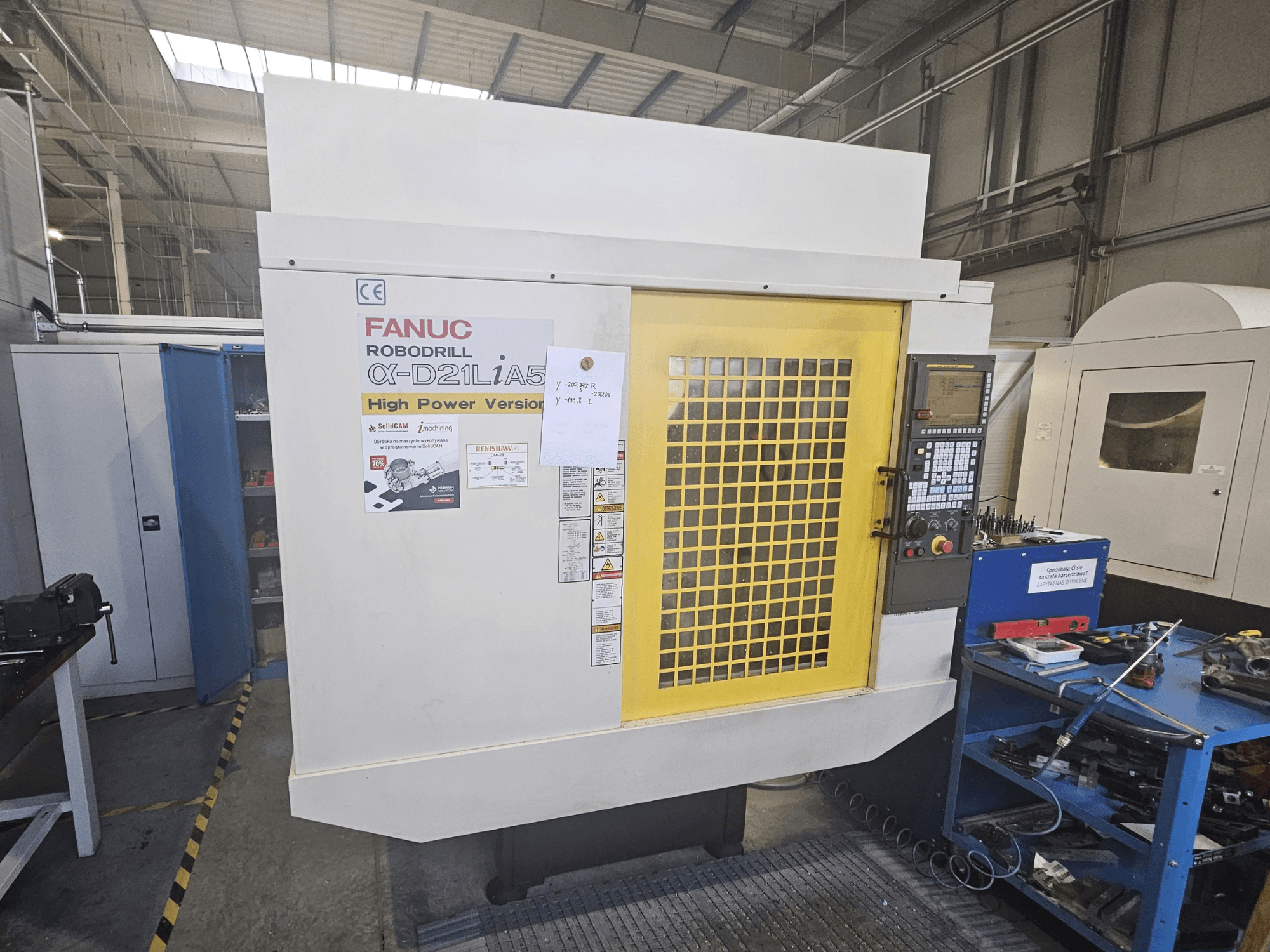 Вид спереди на рободрель FANUC Robodrill α-D21LiA5 с желтой защитной дверцей, панелью управления и инструментами в рабочей зоне.