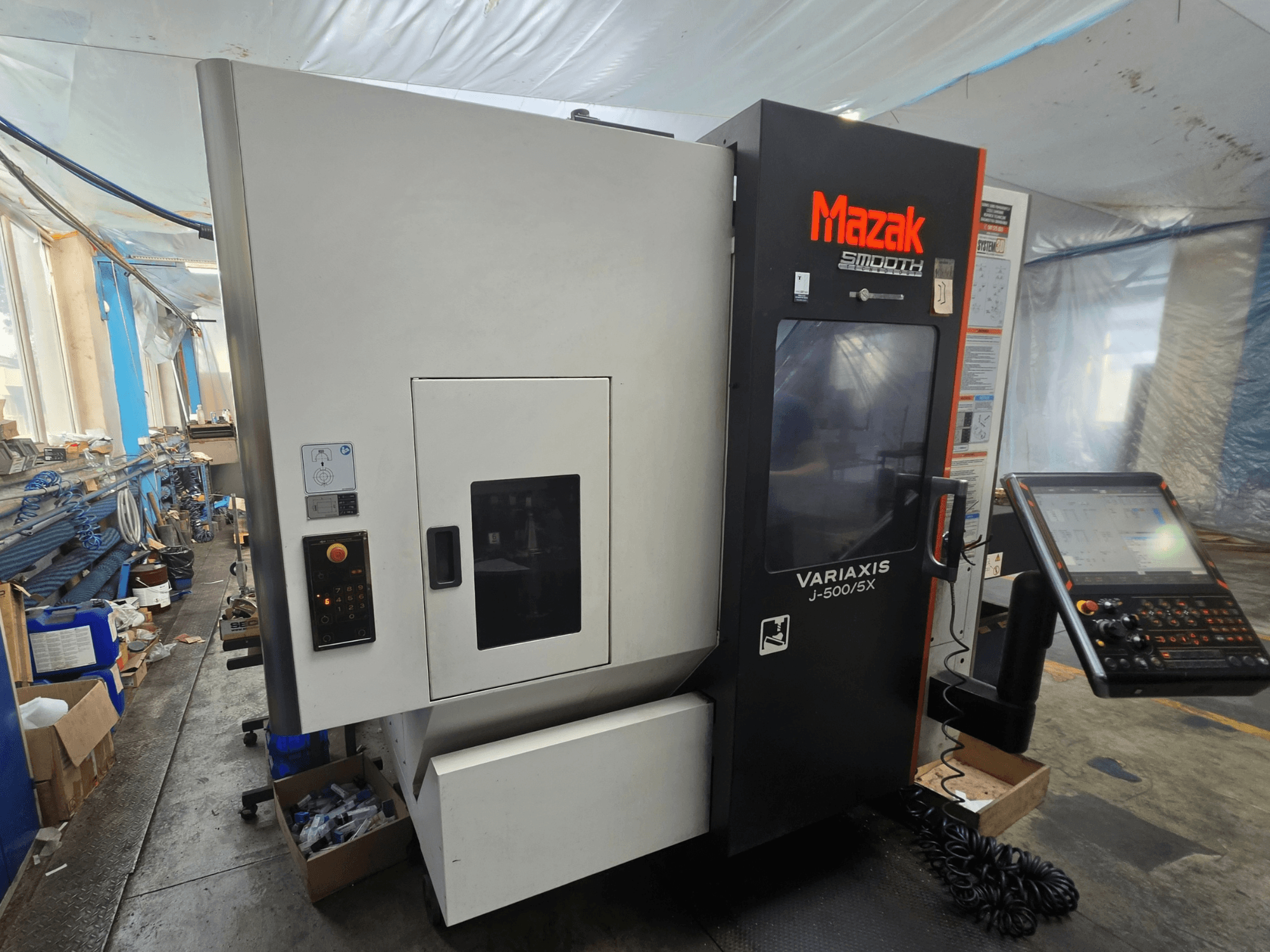 Вертикальный обрабатывающий центр Mazak VARIAXIS J-500/5X, вид сбоку с изображением органов управления и дисплея, установленный в условиях цеха.