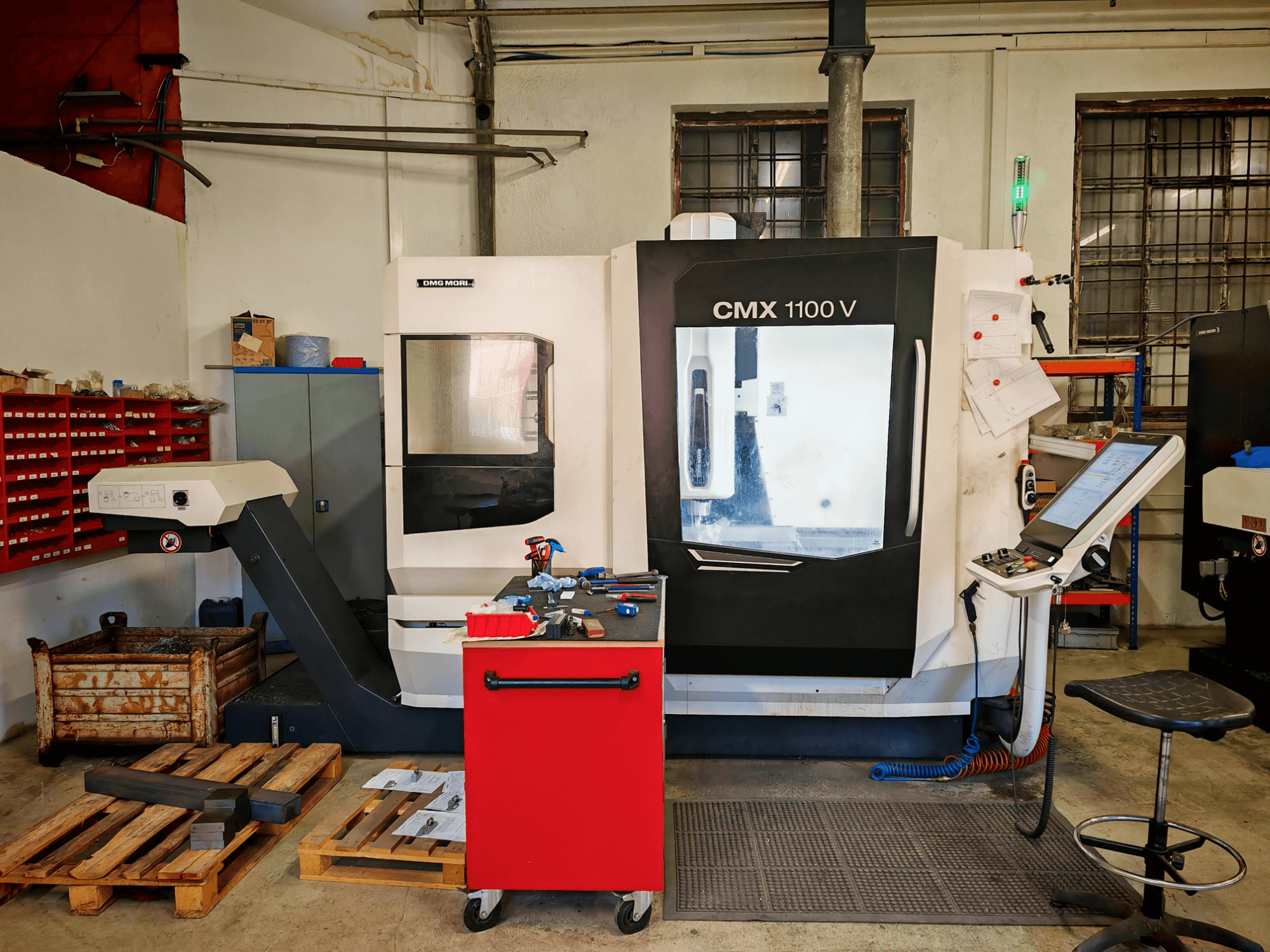 Вертикальный обрабатывающий центр DMG MORI CMX 1100 V в цехе, вид спереди, на котором видны панель управления и расположенные вокруг него инструменты.