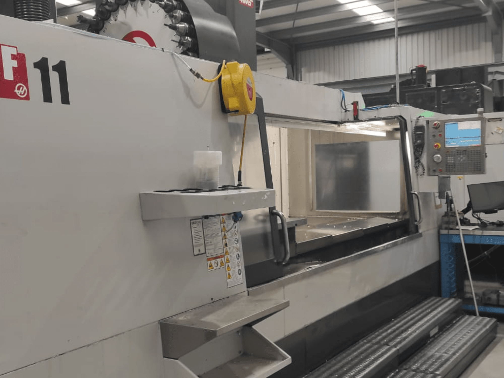 Станок Haas, модель VF-11, показан спереди, видны панель управления, большая рабочая зона и знаки безопасности.