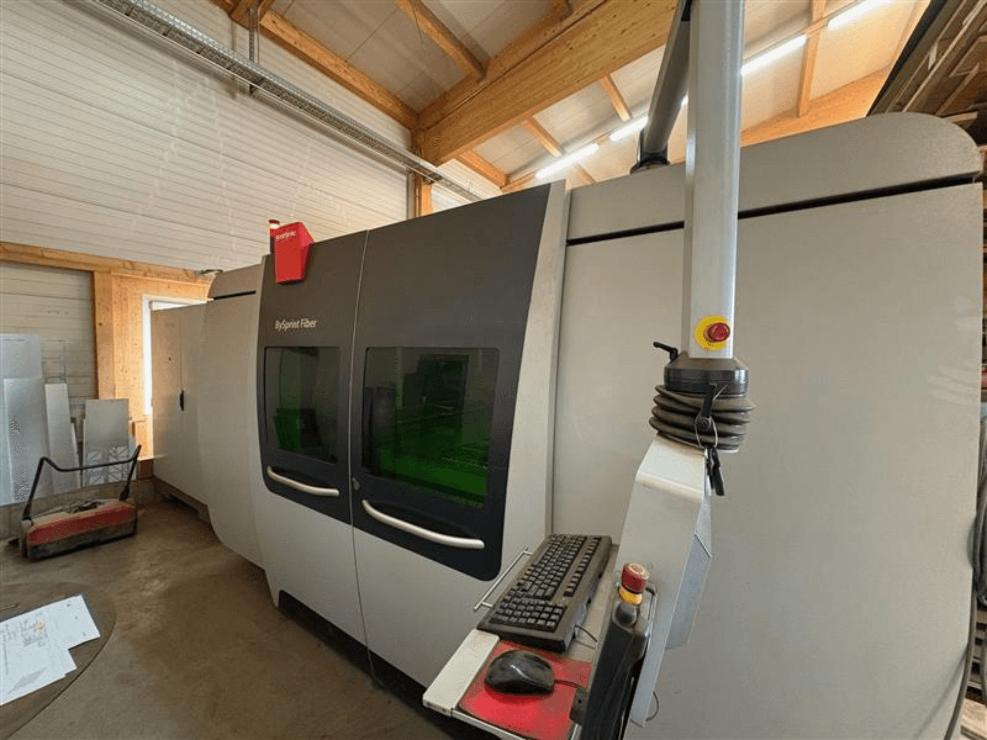 Машина для резки волокна Bystronic ByJet Fiber в мастерской, вид спереди, показывающий панель управления и двойные зеленые смотровые окна.