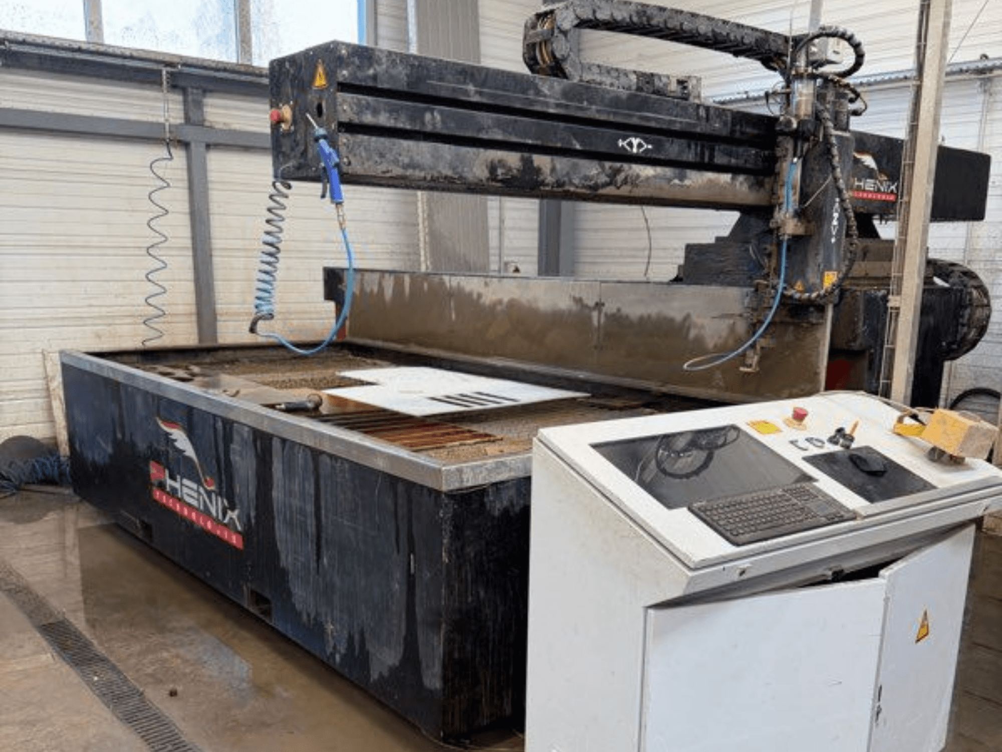 Станок гидроабразивной резки PHENIX MD JET 1530, вид спереди, показывающий панель управления и зону резки с видимым баком для воды.