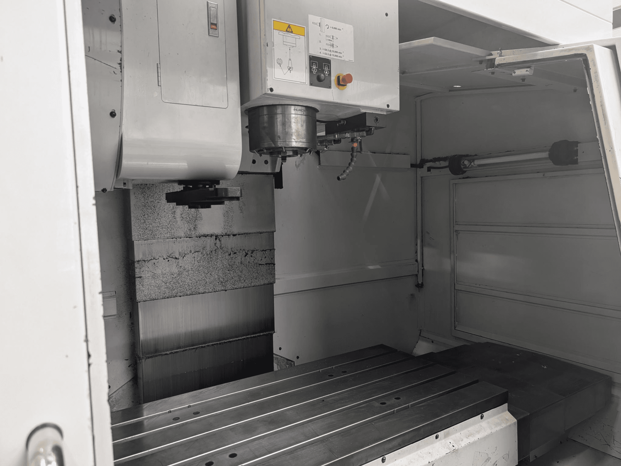 Вид изнутри фрезерного станка с ЧПУ с большим металлическим рабочим столом и двигателем шпинделя, с подробным описанием компонентов и панели управления.