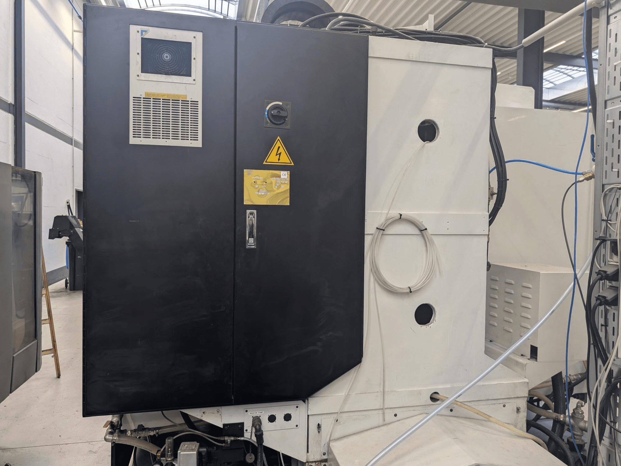 Черная панель управления промышленной машины с предупреждающими надписями, видимыми вентиляционными отверстиями и проводкой. Вид сбоку, демонстрирующий дизайн и особенности.