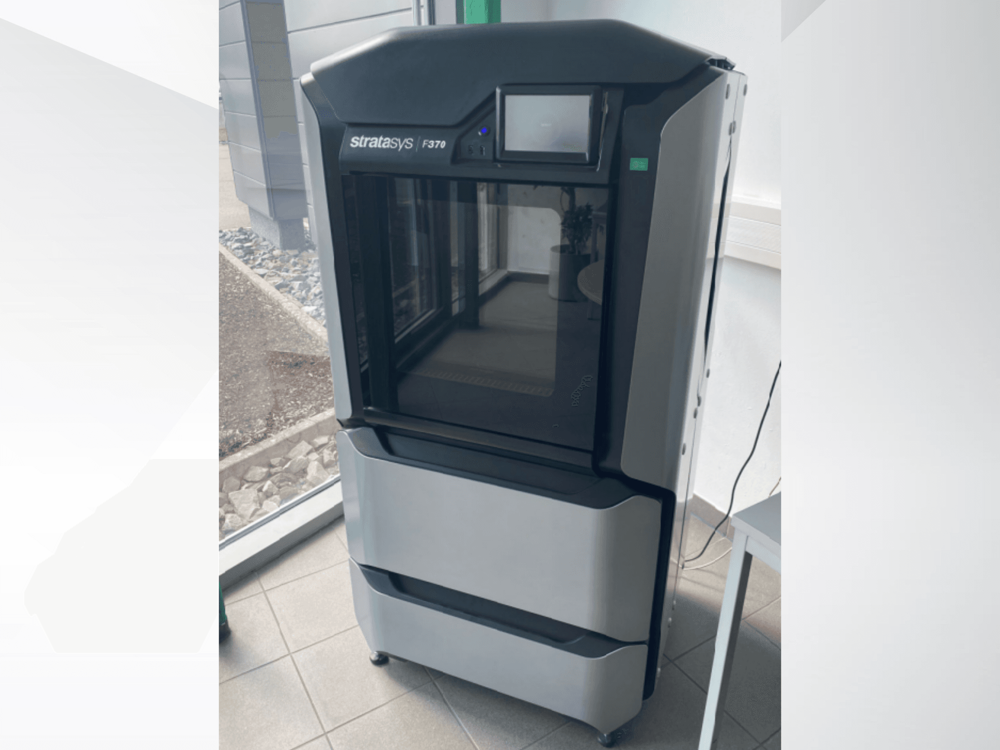 Пластиковый 3D-принтер Stratasys F370, вид спереди, демонстрирует элегантный черно-серый дизайн с сенсорным дисплеем.