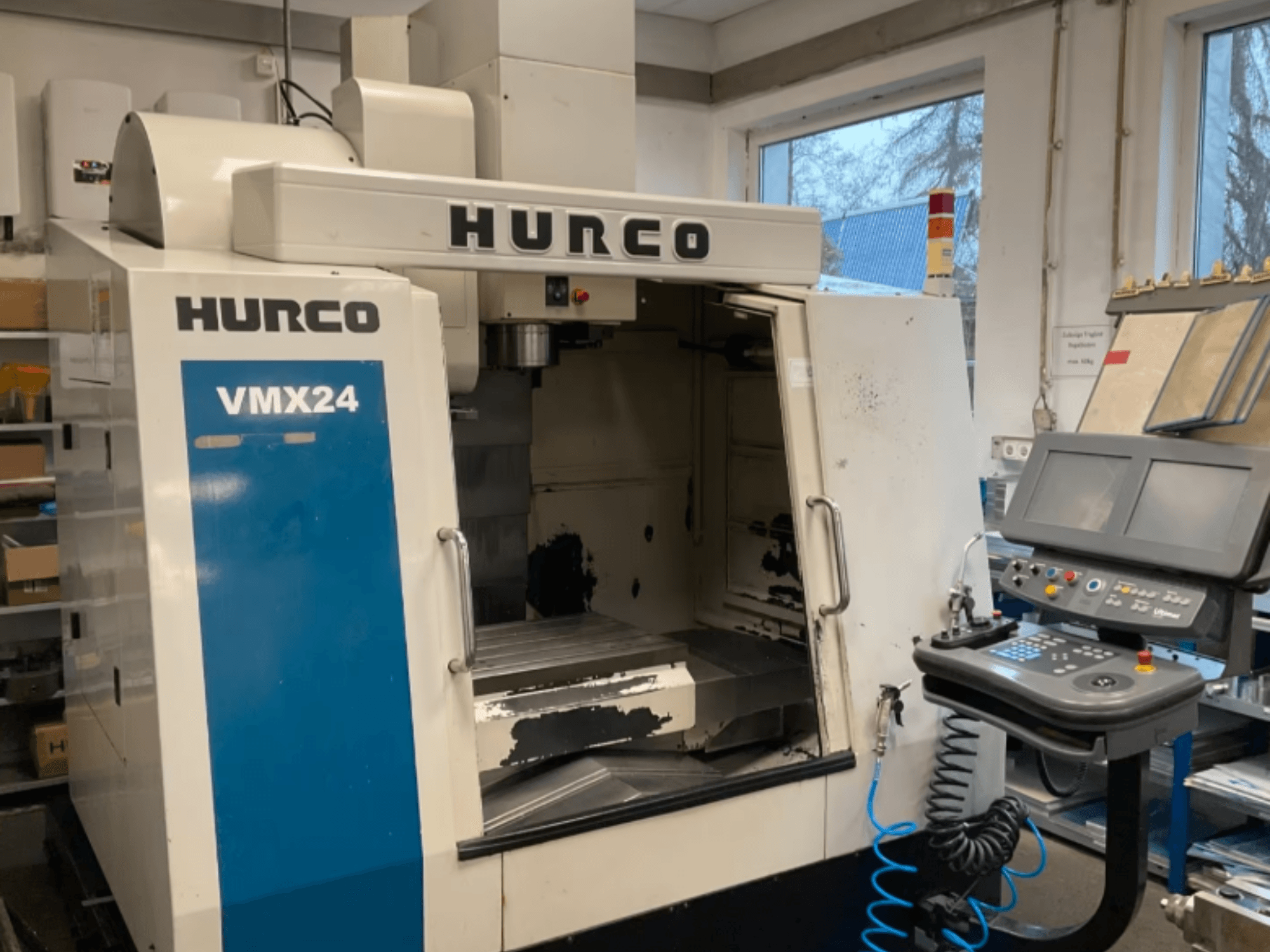 Вертикальный обрабатывающий центр Hurco VMX24 в виде спереди, на котором видны панель управления, шпиндельная головка и рабочая зона; заметны следы износа.