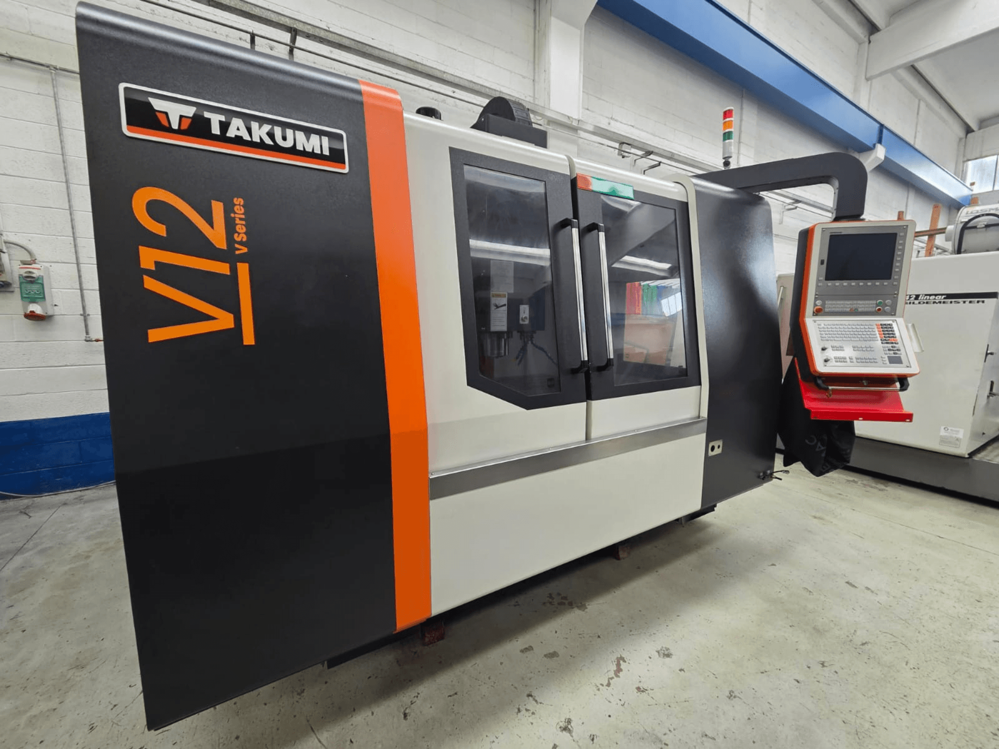 Фрезерный станок с ЧПУ Takumi V12 серии V, вид спереди, имеет панель управления и большие стеклянные окна.