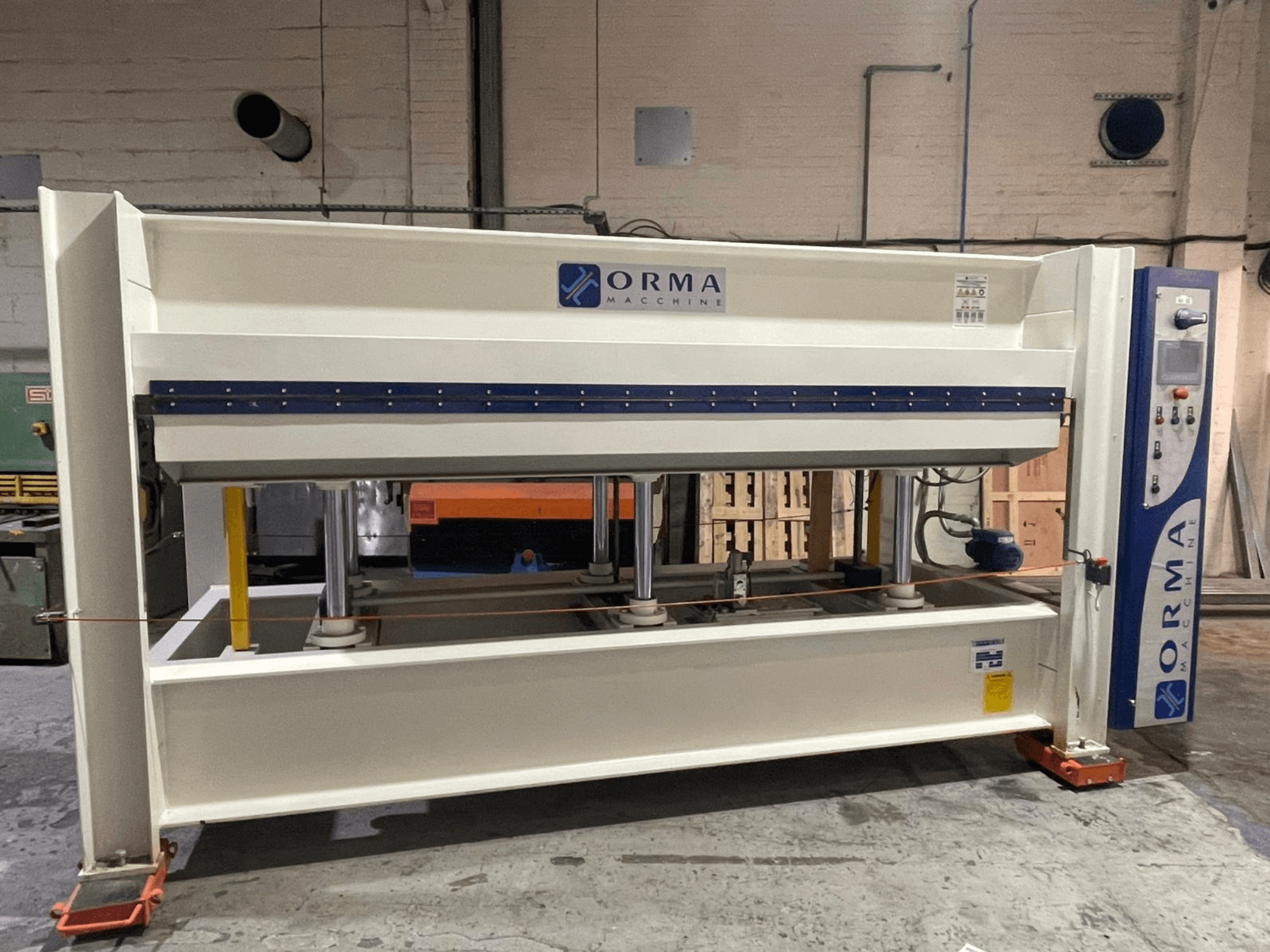 Гидравлический пресс ORMA machinery, вид спереди, с серебристой отделкой, панелью управления справа и вертикальными поршнями для прессования.