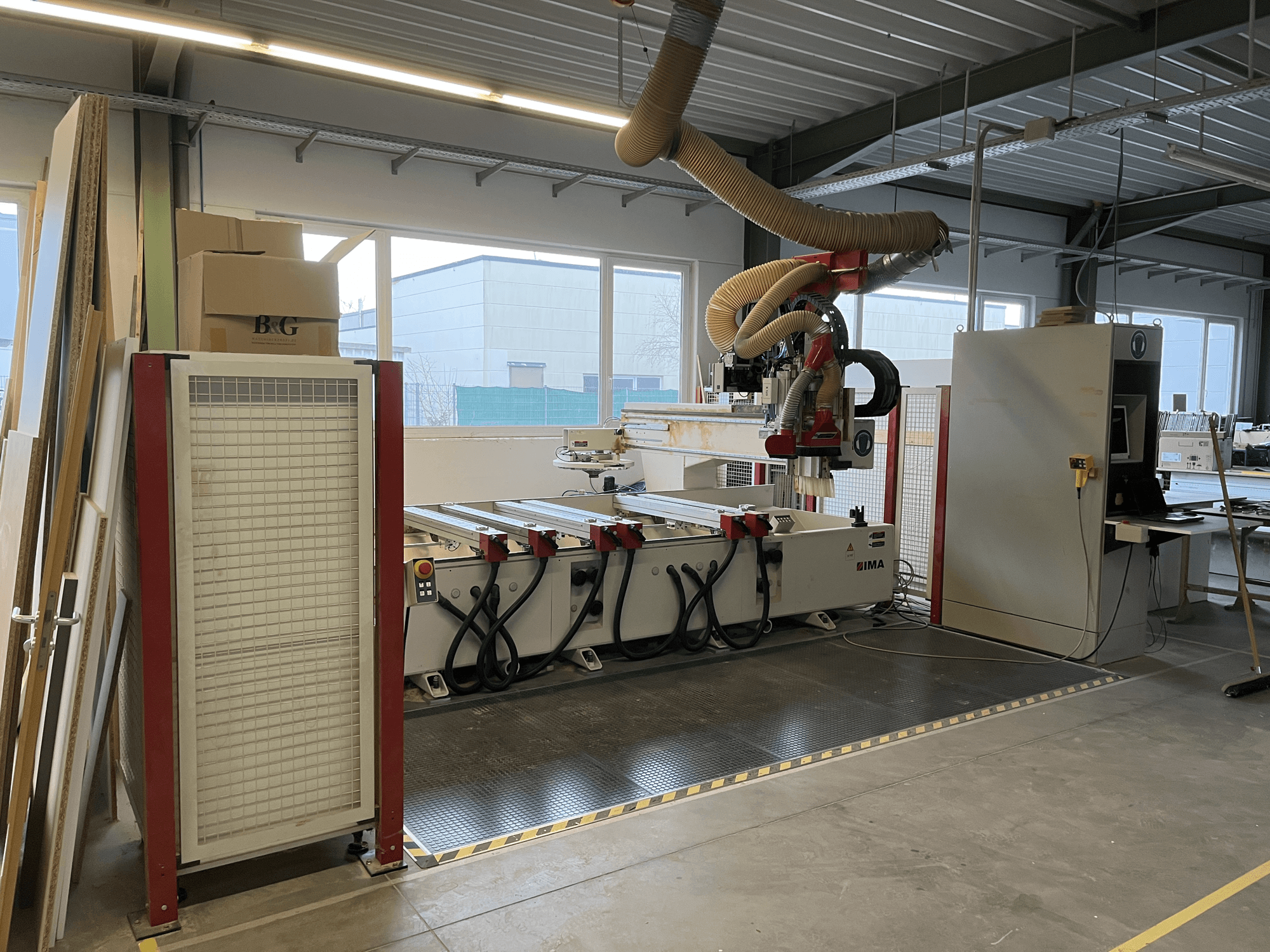 Деревообрабатывающий центр с ЧПУ IMA BIMA 410 в мастерской, вид сбоку, видна панель управления и система пылеудаления.