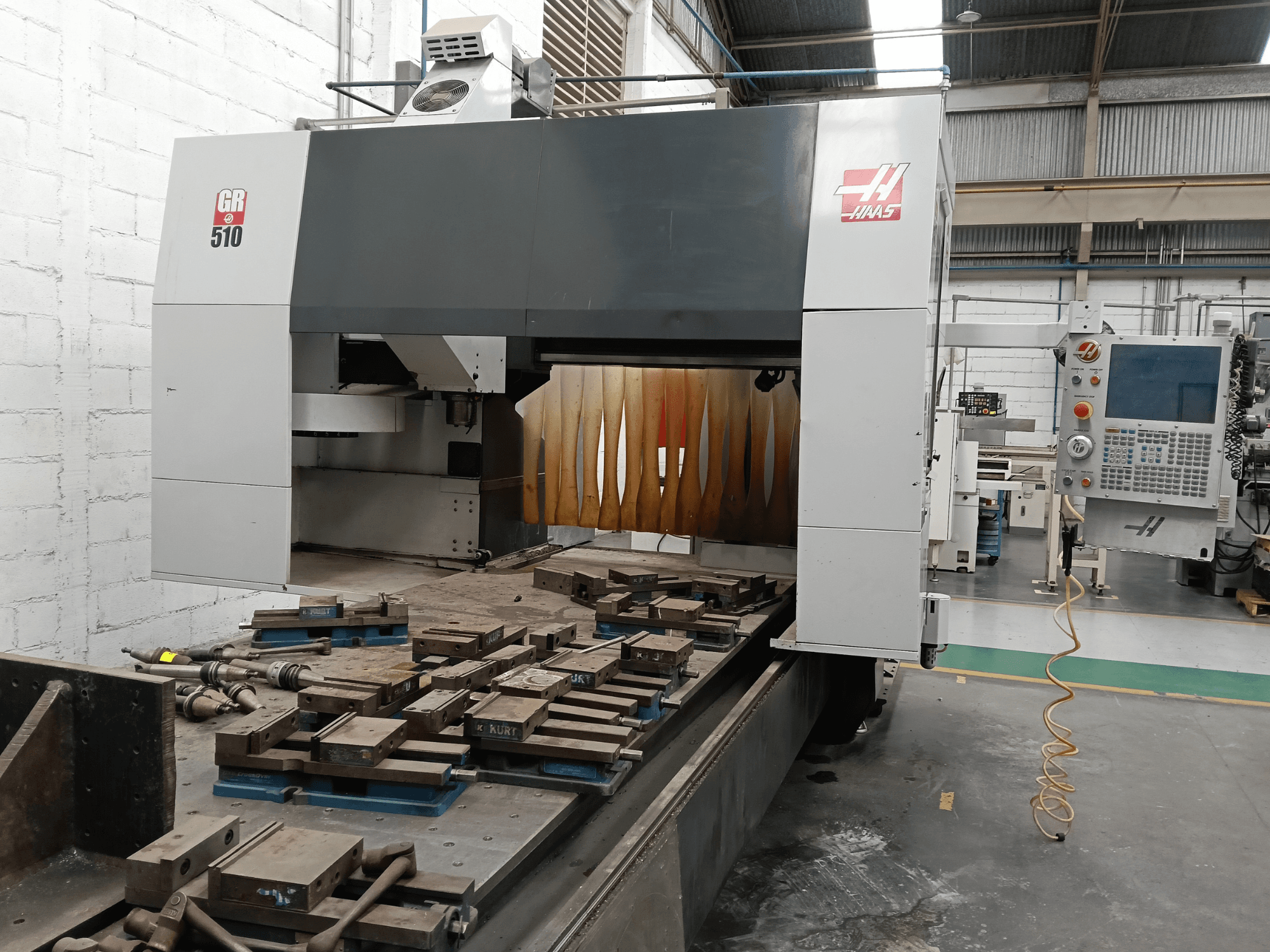 Вид спереди на портальный фрезерный станок HAAS GR-510 с панелью управления и обработанными деталями на столе.