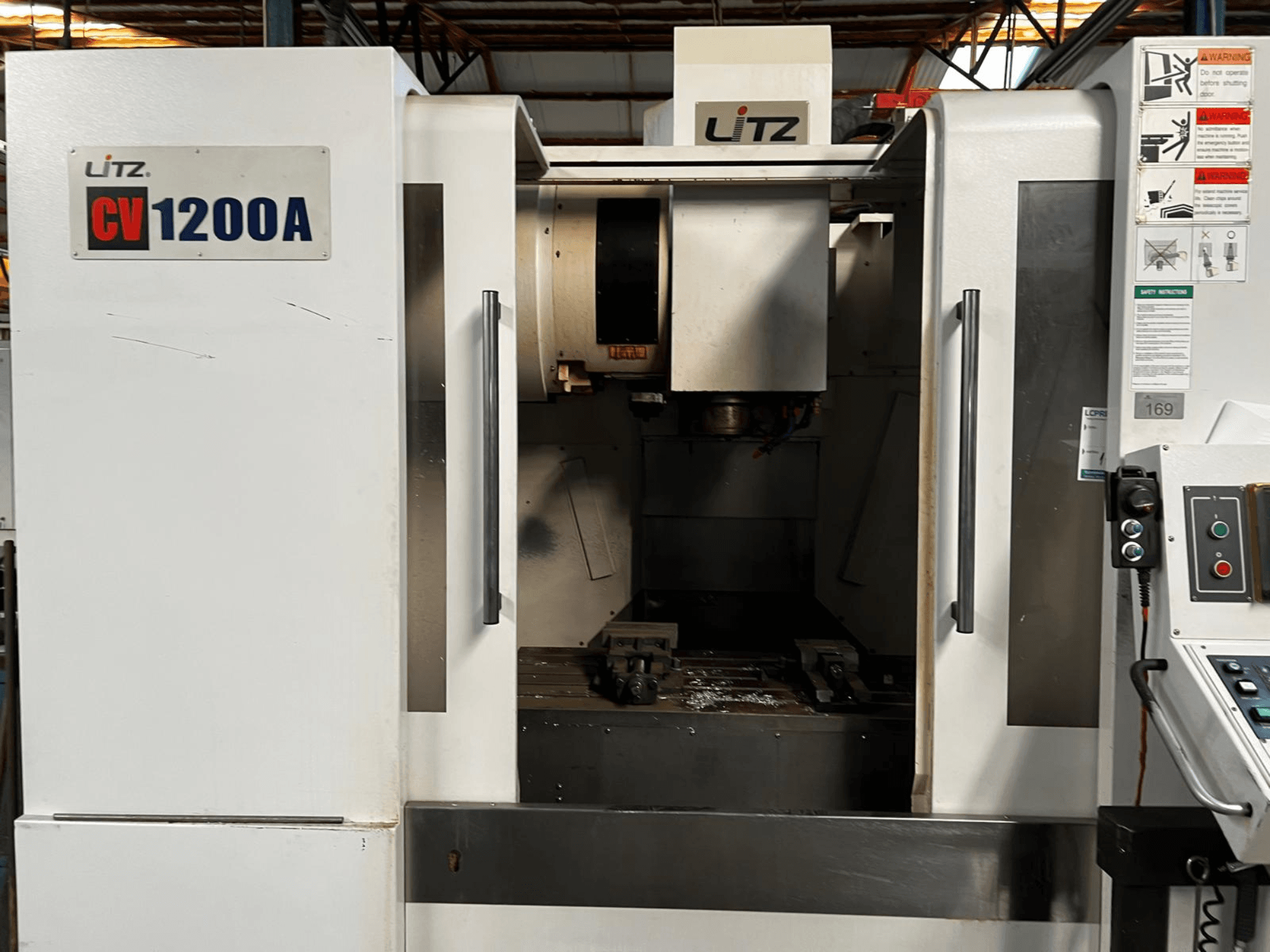 Вертикальный обрабатывающий центр Litz CV1200A, вид спереди, на котором видны панель управления, шпиндель и открытая дверца, открывающая вид на рабочую зону.