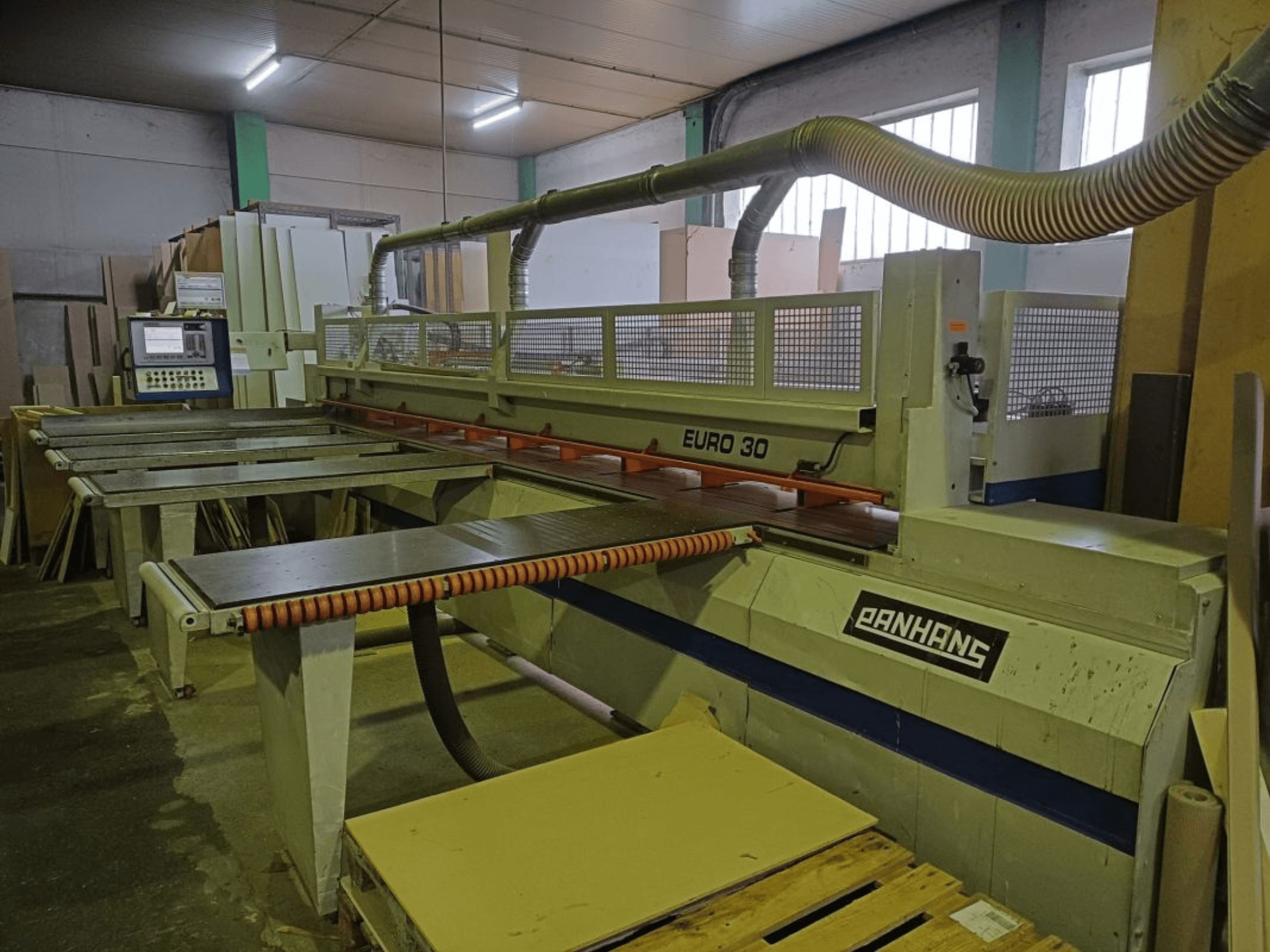 Вид спереди панельной пилы PANHANS EURO 30 с панелью управления, режущим столом и шлангом для удаления пыли в мастерской.