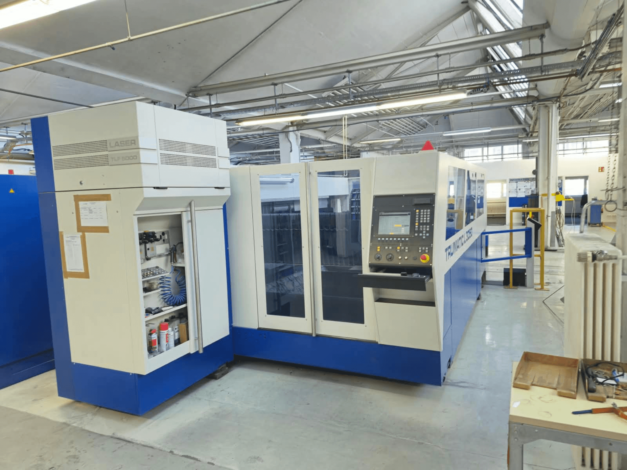 Лазерный резак TRUMPF TruLaser L3050 с CO₂-лазером, вид спереди, с панелью управления и дверцей для доступа при техническом обслуживании, в заводской комплектации.