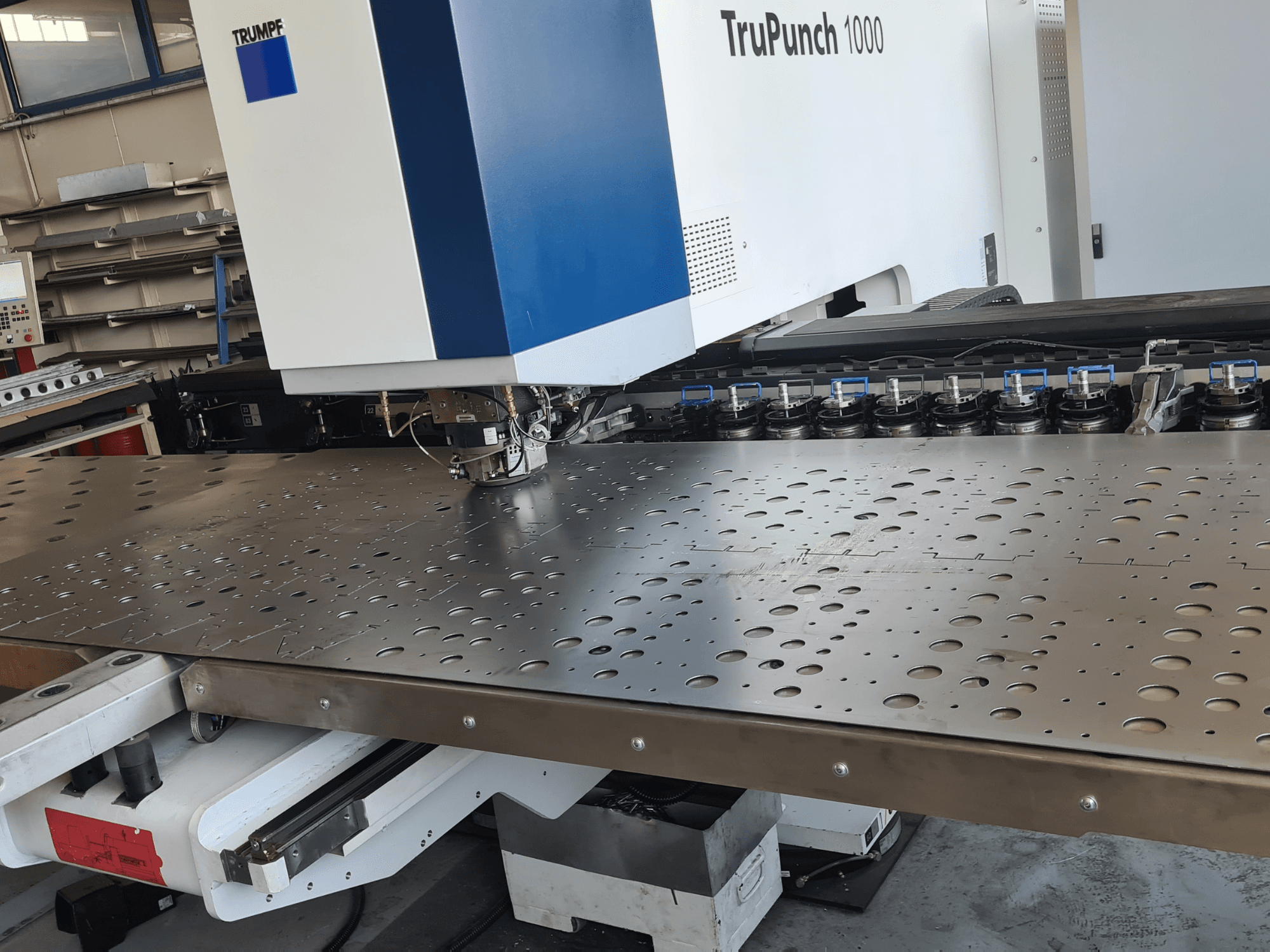 Штамповочный станок с ЧПУ TRUMPF TruPunch 1000, вид спереди, с перфорированным металлическим листом и установленным инструментом.