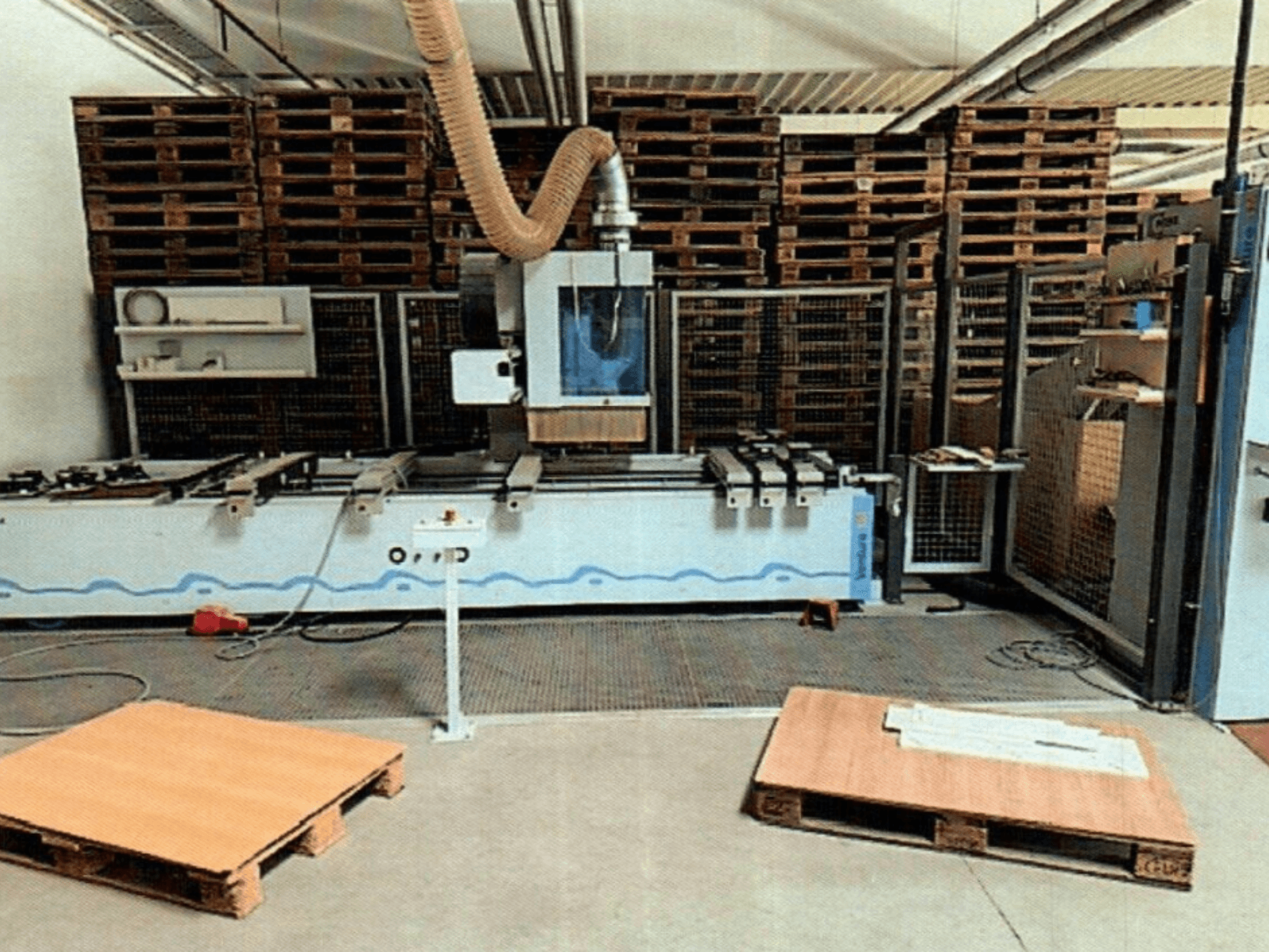 Деревообрабатывающий центр с ЧПУ Weeke Venture 1M в мастерской, вид спереди, видны деревянные поддоны и промышленная установка.