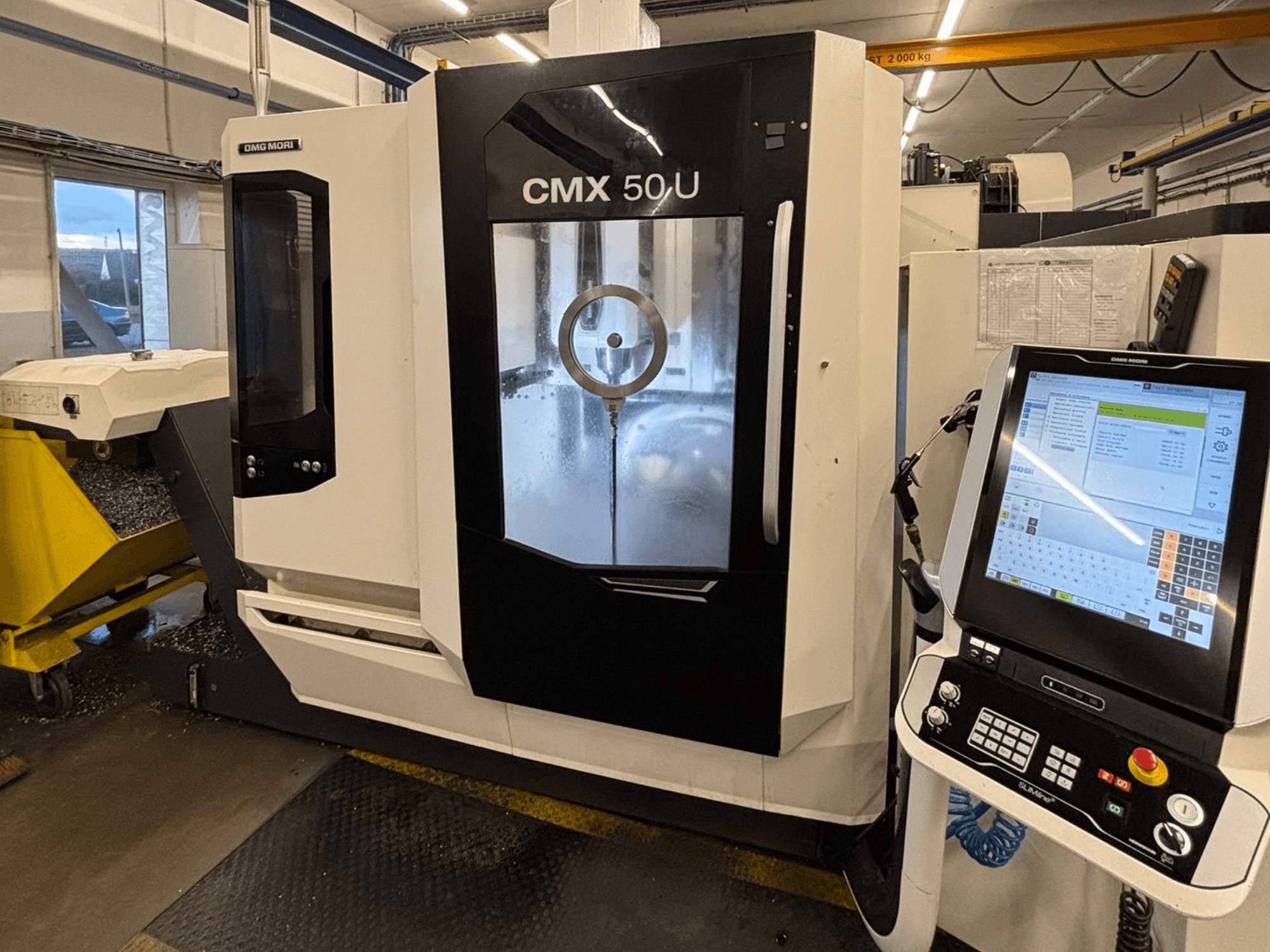 Вертикальный обрабатывающий центр DMG MORI CMX 50 U, вид спереди с панелью управления и стеклянным дисплеем, демонстрирующим внутреннюю механику.