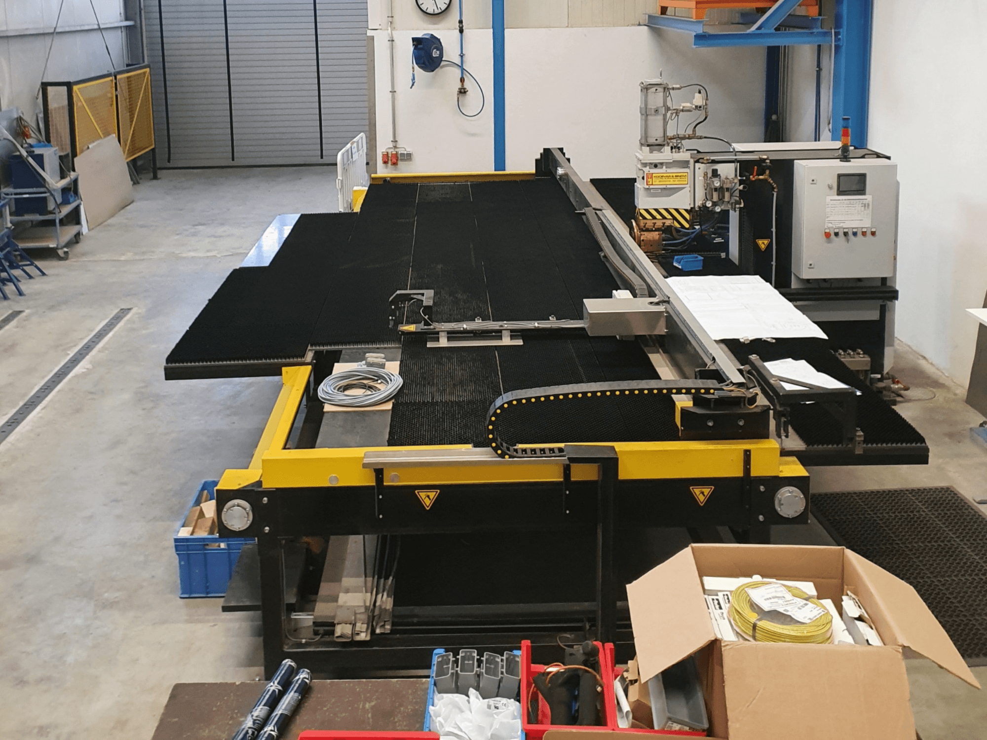 Промышленный режущий станок с желтыми и черными элементами, вид спереди, с изображением органов управления и принадлежностей в заводских условиях.