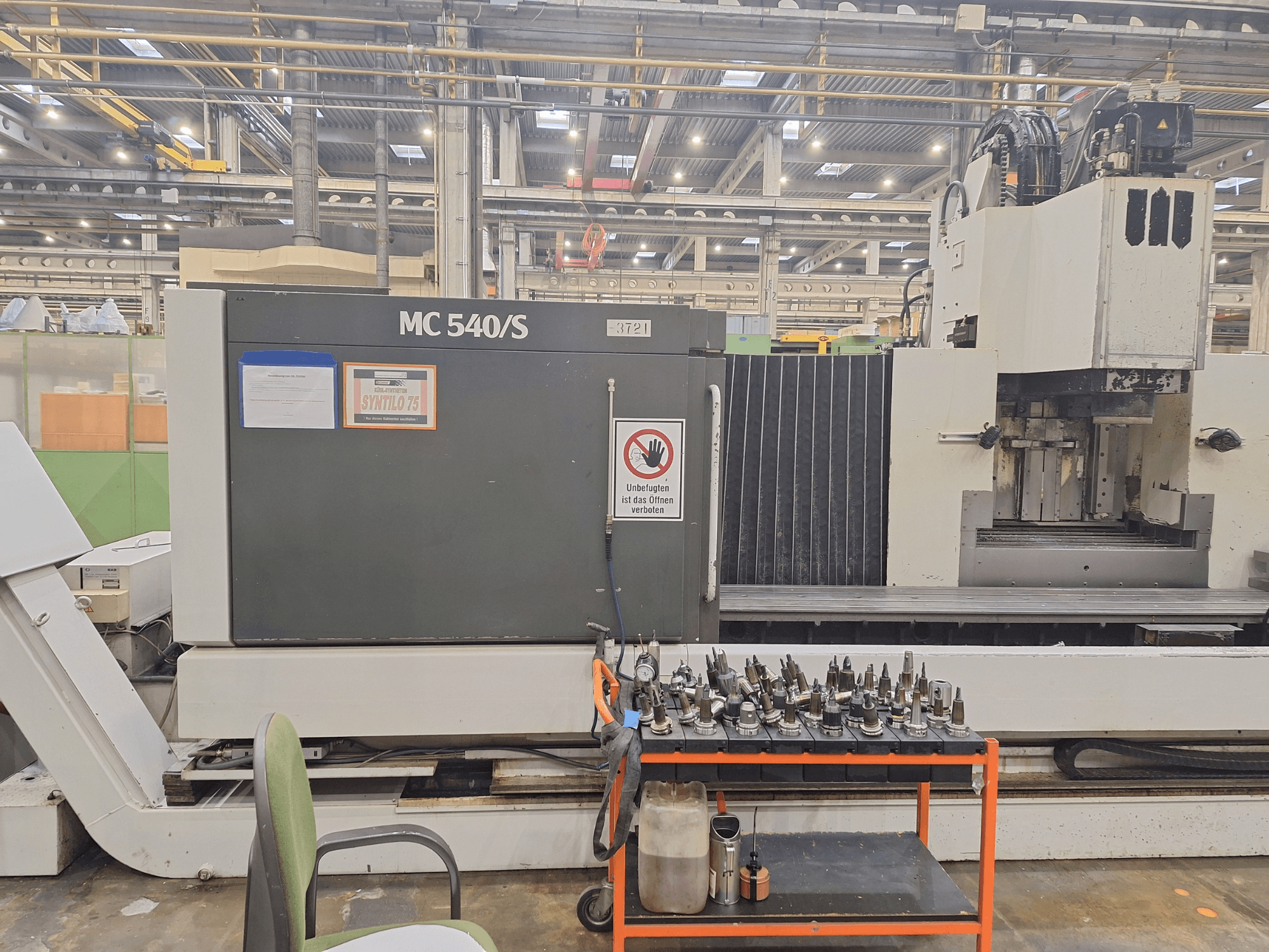 Вертикальный обрабатывающий центр STAMA MC 540S в мастерской, вид сбоку с держателями инструментов на тележке рядом.