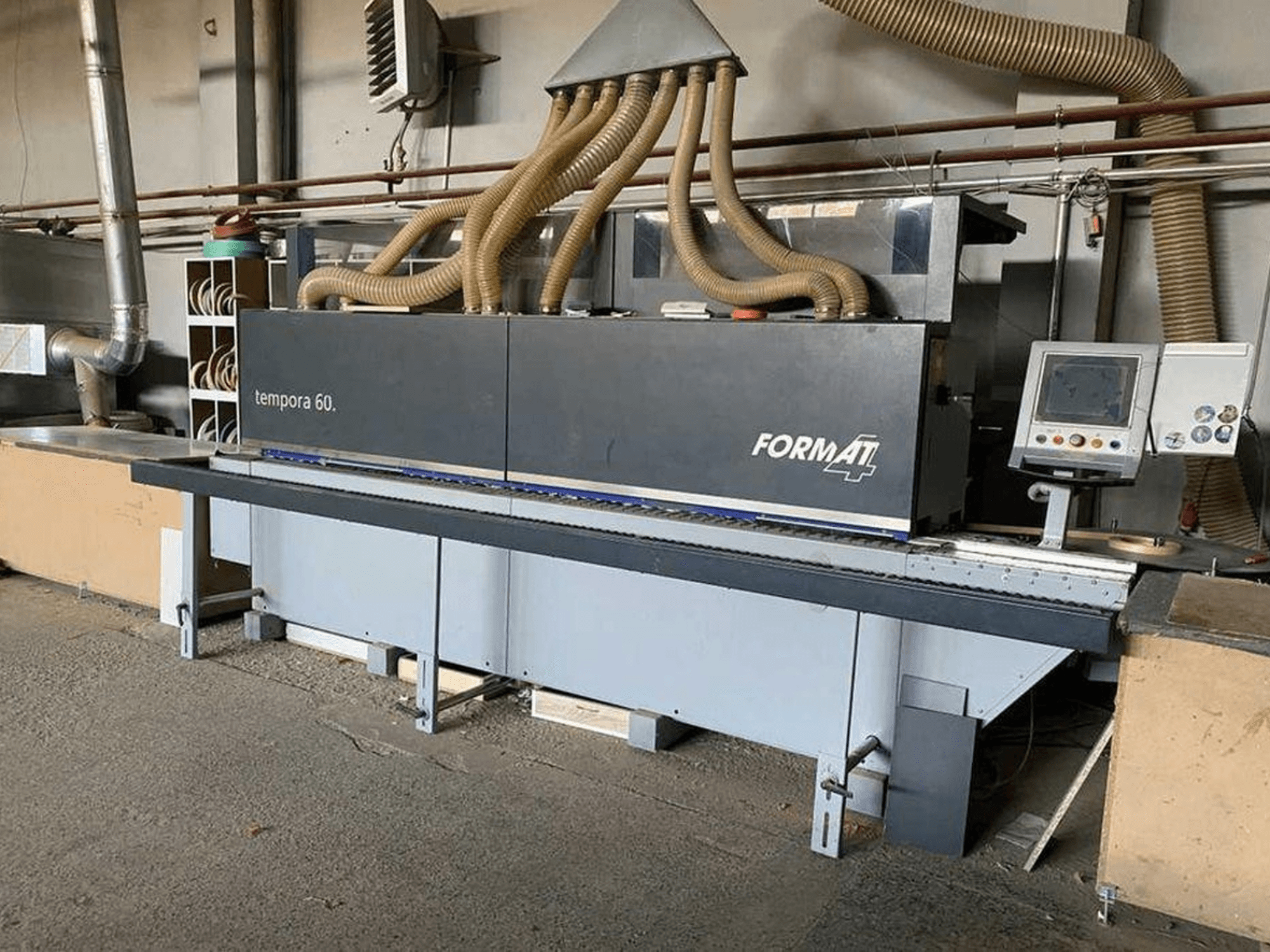 Кромкооблицовочный станок FORMAT4 Tempora 60 с видом сбоку, с многочисленными шлангами и панелью управления с кнопками и экраном.