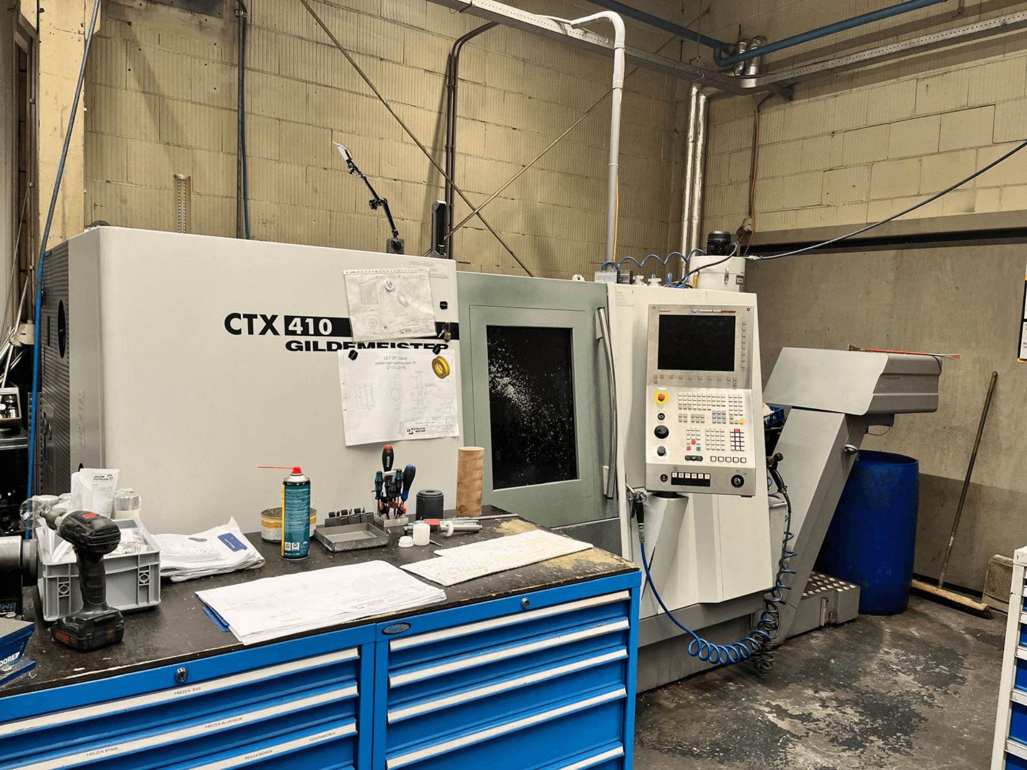Станок с ЧПУ Gildemeister CTX 410 в мастерской, вид спереди, панель управления и различные инструменты на верстаке.