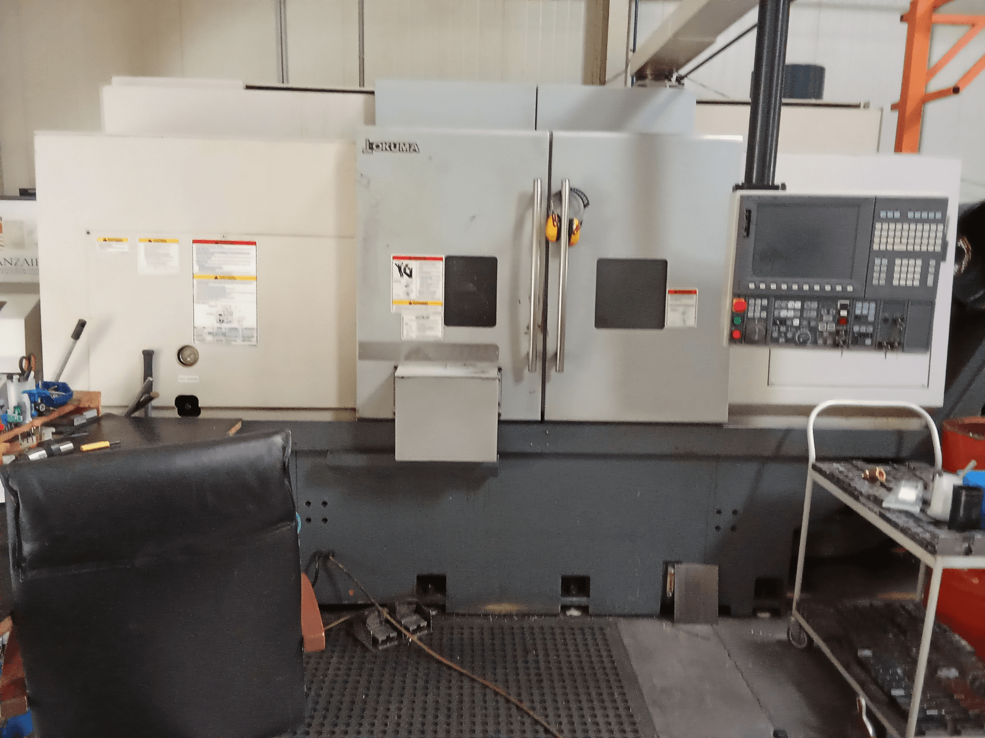Горизонтальный токарный станок Okuma Genos L300 E-M с видом спереди, панель управления и двойные двери, установленные в мастерской.