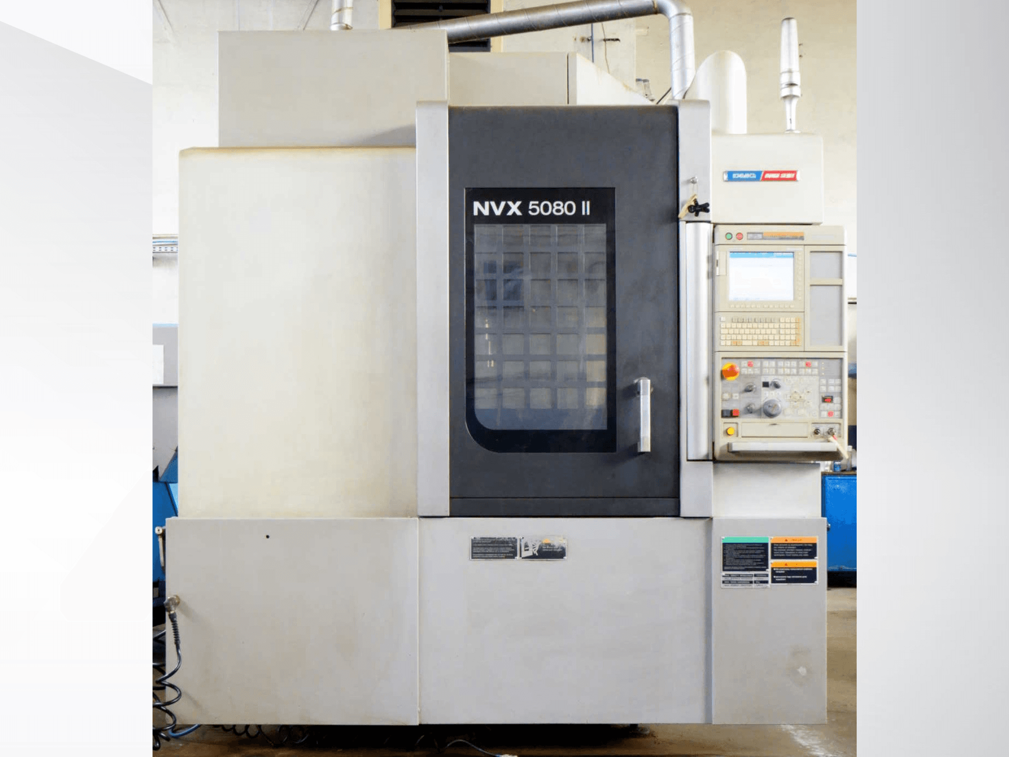 Вертикальный обрабатывающий центр DMG Mori Seiki NVX 5080 II, вид спереди, с панелью управления и решетчатой дверцей.