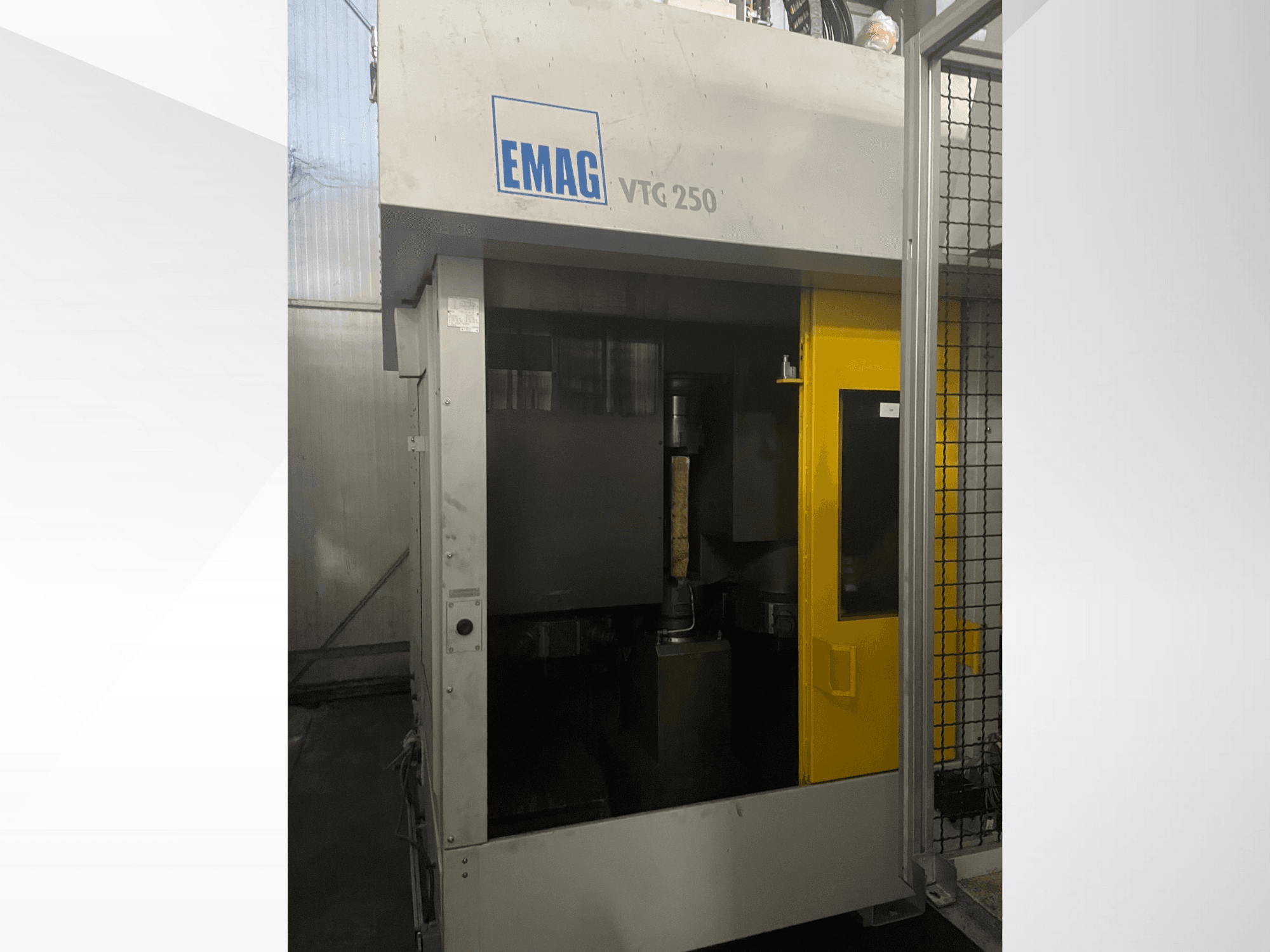 Вертикальный обрабатывающий центр EMAG VTC 250 на переднем плане, с желтой дверью и видимым режущим инструментом внутри камеры.