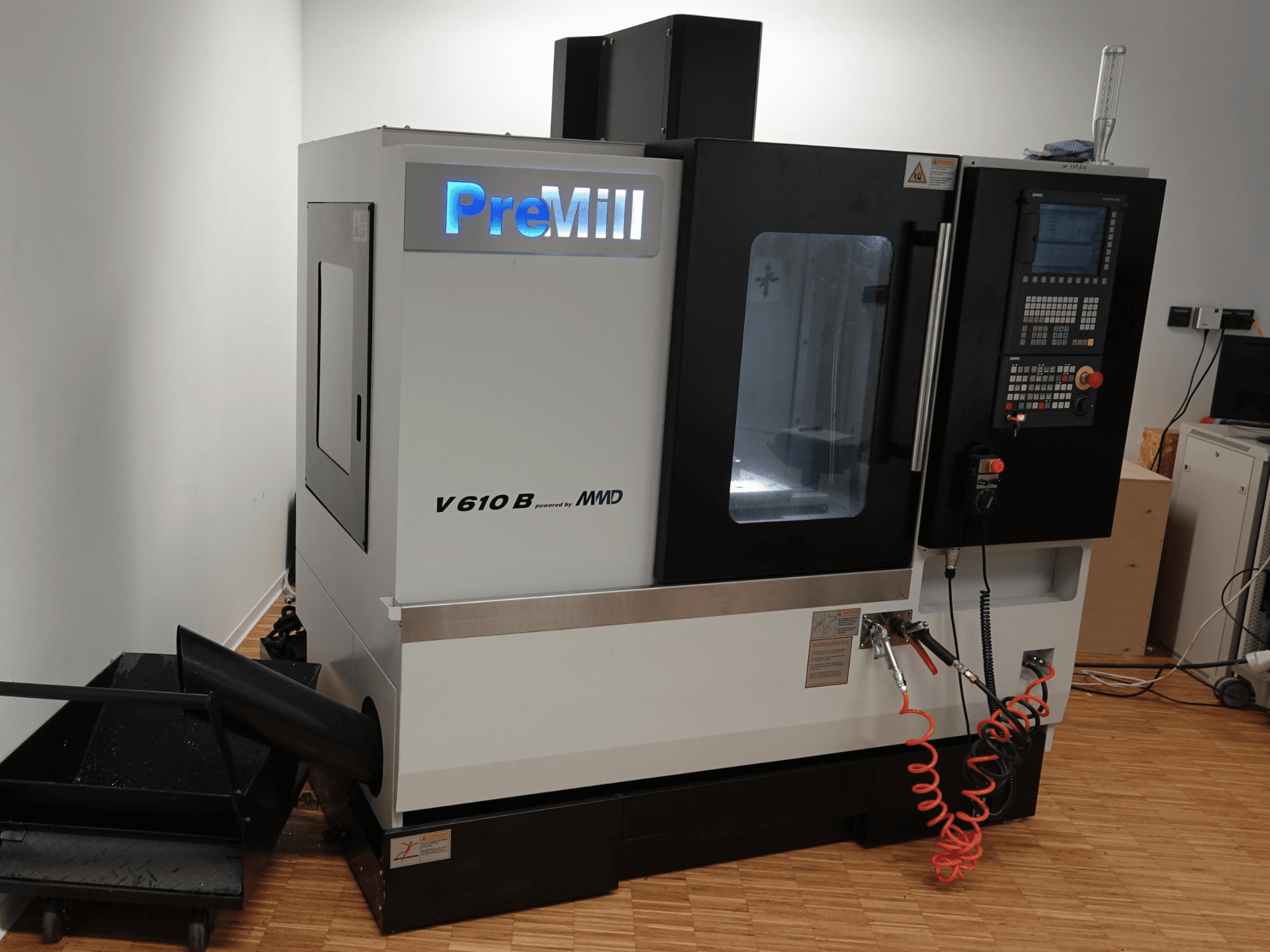 Вертикальный обрабатывающий центр PreMill V 610 B, вид спереди, с панелью управления, системой охлаждения и подсоединенными воздушными шлангами.