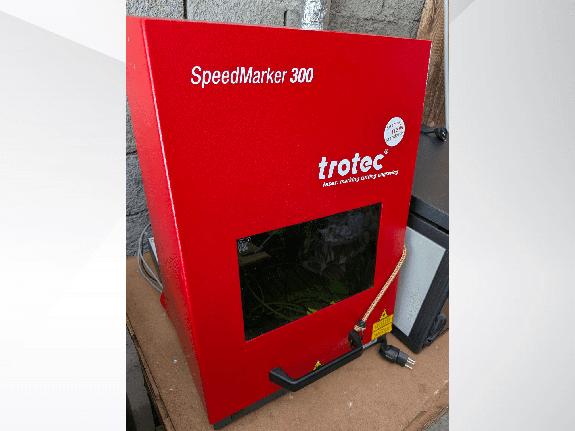 Красная лазерная маркировочная машина Trotec SpeedMarker 300 с видом спереди, с большим смотровым окном и подключением питания.