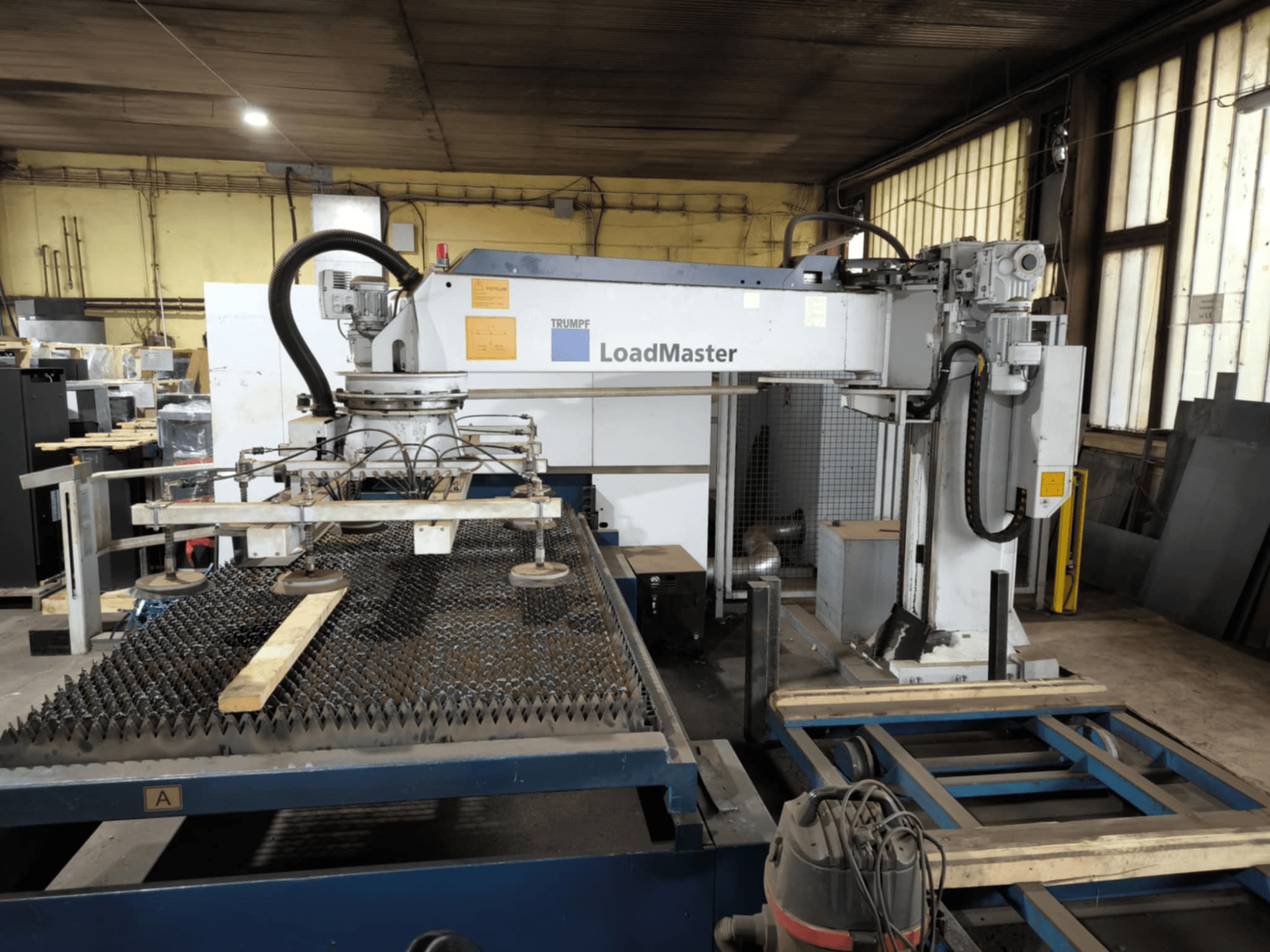 Машина для резки волокна TRUMPF TRULASER 3030, вид спереди, демонстрирует систему LoadMaster и располагается на решетчатом рабочем столе.