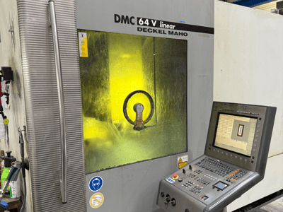 Линейная машина DMC 64 V от Deckel Maho, вид спереди с панелью управления и желтым тонированным окошком, показывающим внутренние механизмы.