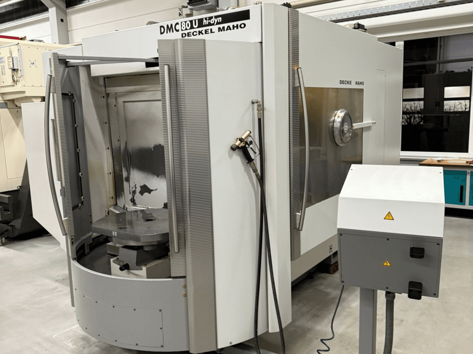 Вид спереди на высокоскоростной фрезерный станок с ЧПУ Deckel Maho DMC 80 U с открытой дверцей и панелью управления сбоку.