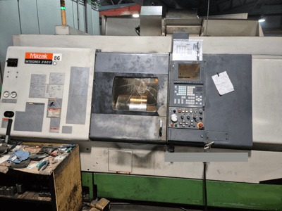 Токарный станок Mazak Integrex 200Y, вид спереди, с панелью управления и инструментами на столе. Видны манометры и экран дисплея.
