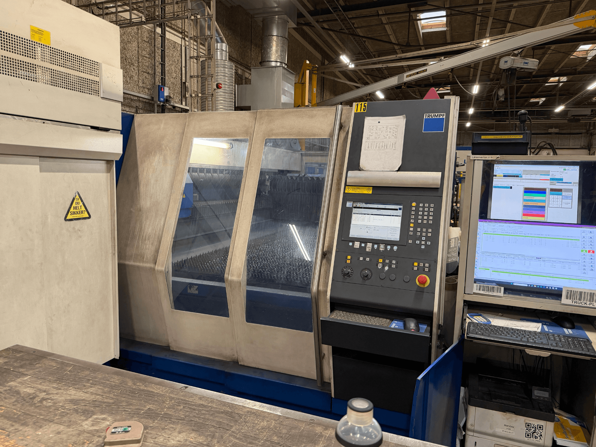 Вид спереди на промышленный лазерный станок Trumpf с панелью управления и цифровыми дисплеями, установленный в заводских условиях.